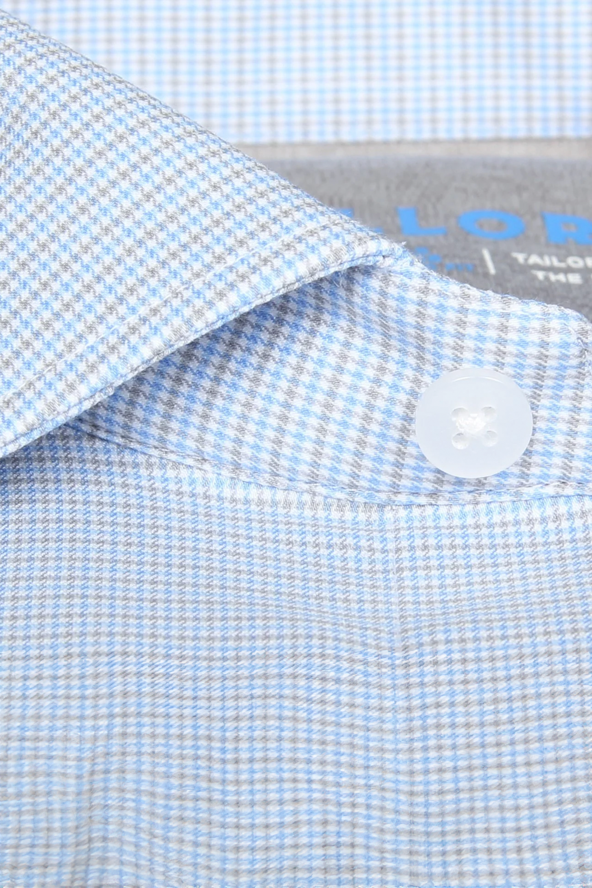 Close-up of the Leader Houndstooth // Grey Blue Performance Shirt collar by Twillory, with a white four-hole button and a gray label. The fabric's texture highlights its 4-way stretch and moisture-wicking features.