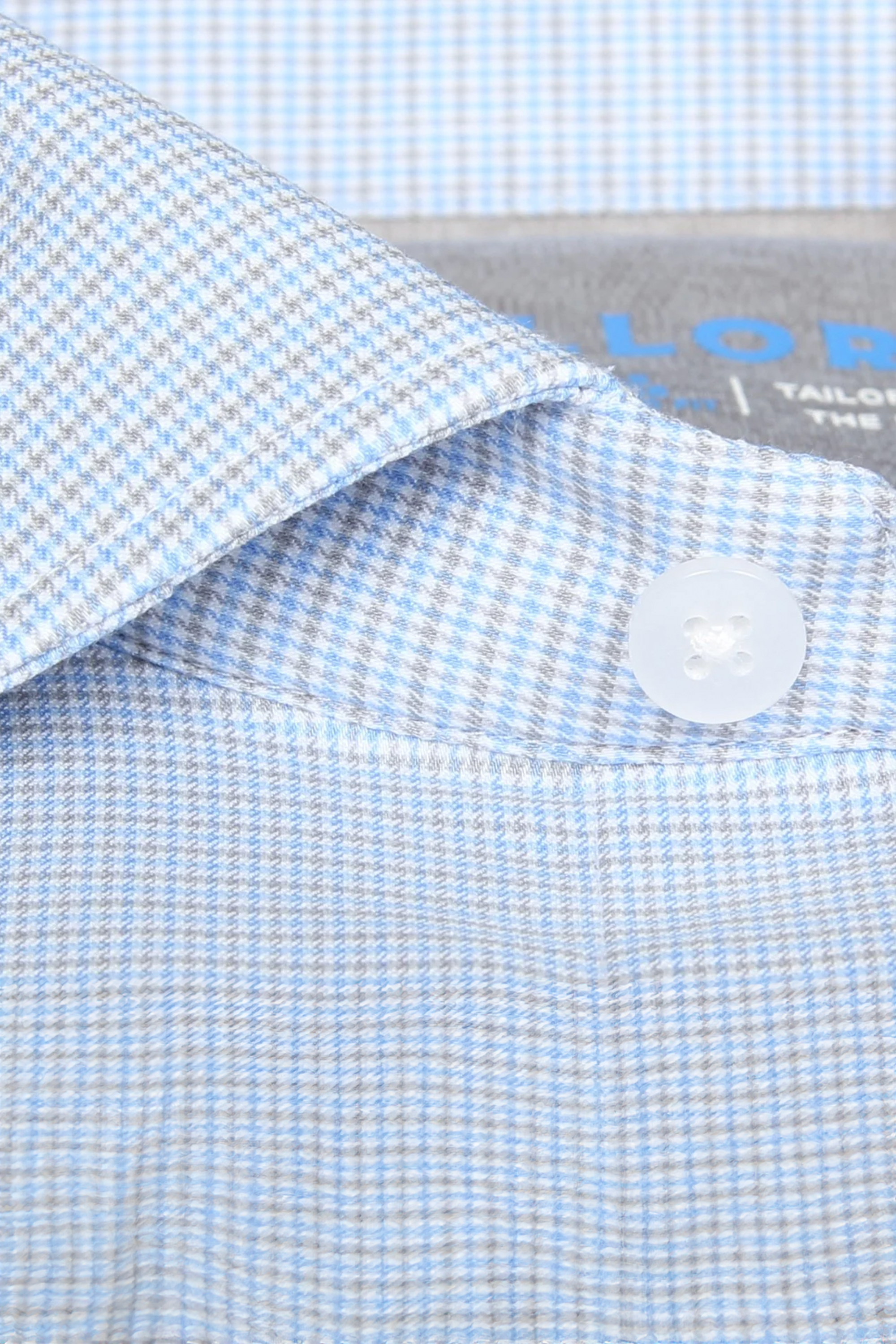 Close-up of the Leader Houndstooth // Grey Blue Performance Shirt collar by Twillory, with a white four-hole button and a gray label. The fabric's texture highlights its 4-way stretch and moisture-wicking features.