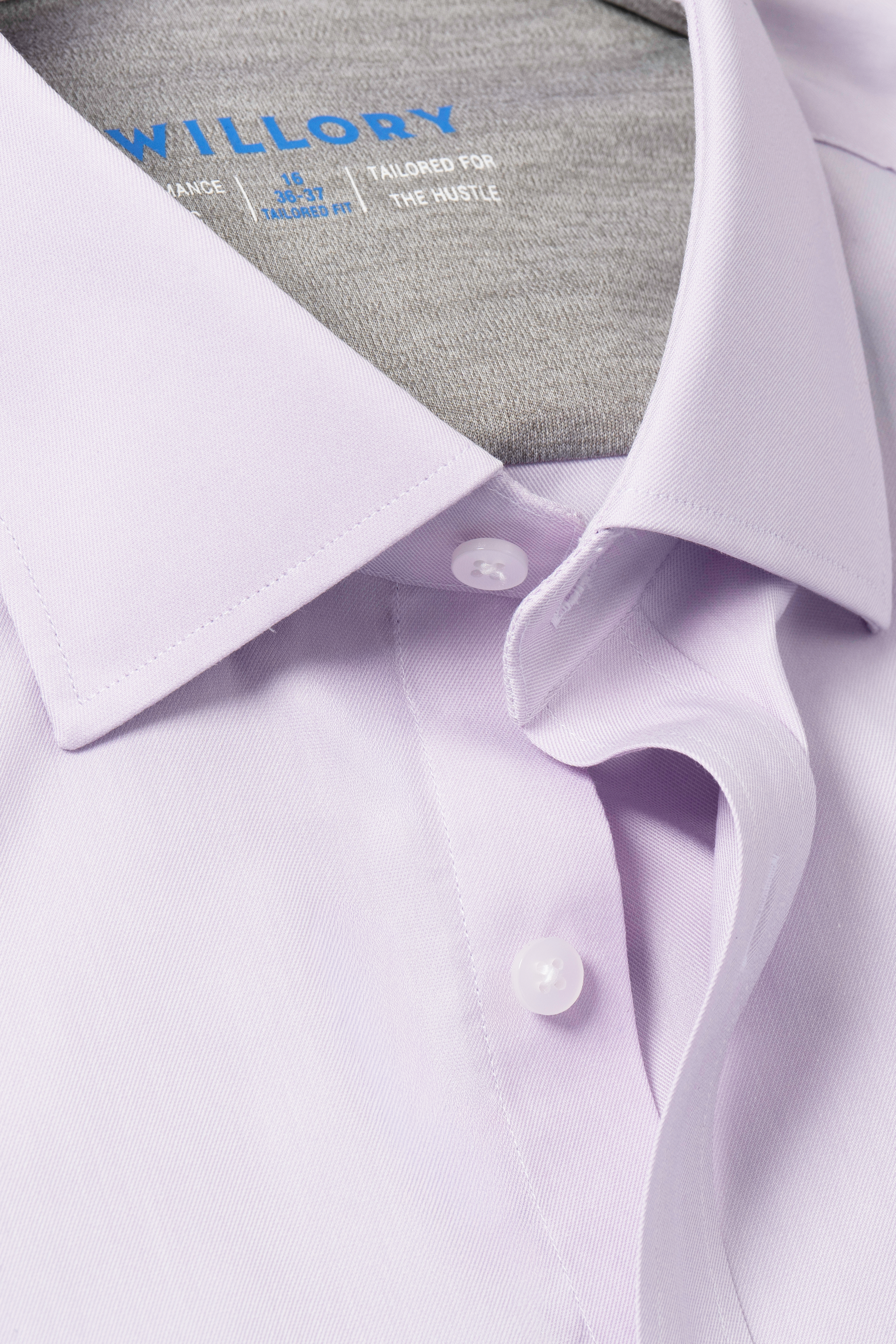 Close-up of the Twillory Leader Solid // Lavender shirt, neatly pressed with a visible collar, two white buttons, part of the placket, and a partially visible blue text neck label on gray. Features comfortable 4-way stretch fabric.