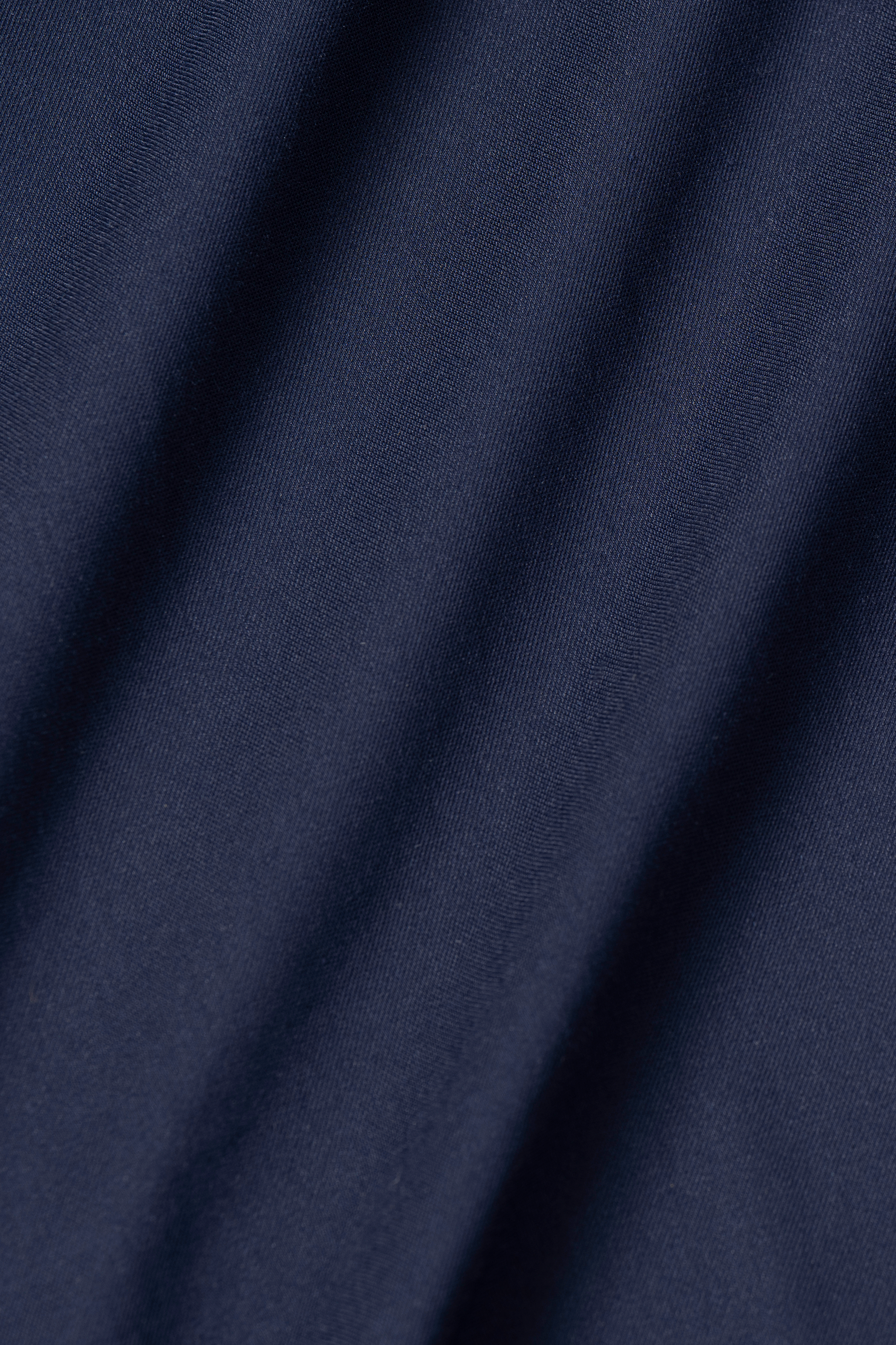 Close-up of Leader Solid // Navy by Twillory: dark blue fabric with diagonal, soft folds casting gentle shadows over a smooth, matte finish. The fine, uniform weave hints at the sleek durability typical of a 4-way stretch performance shirt. No patterns or embellishments.