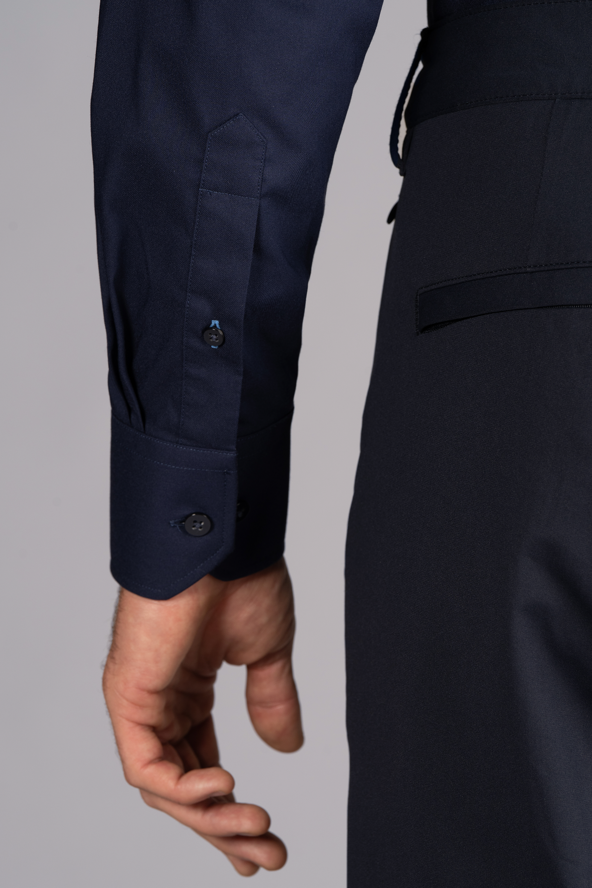 Close-up of a person’s left arm and side, wearing Twillory's Leader Solid // Navy Performance Shirt with 4-way stretch and buttoned cuff, paired with matching dark trousers. A plain background highlights the clothing details.
