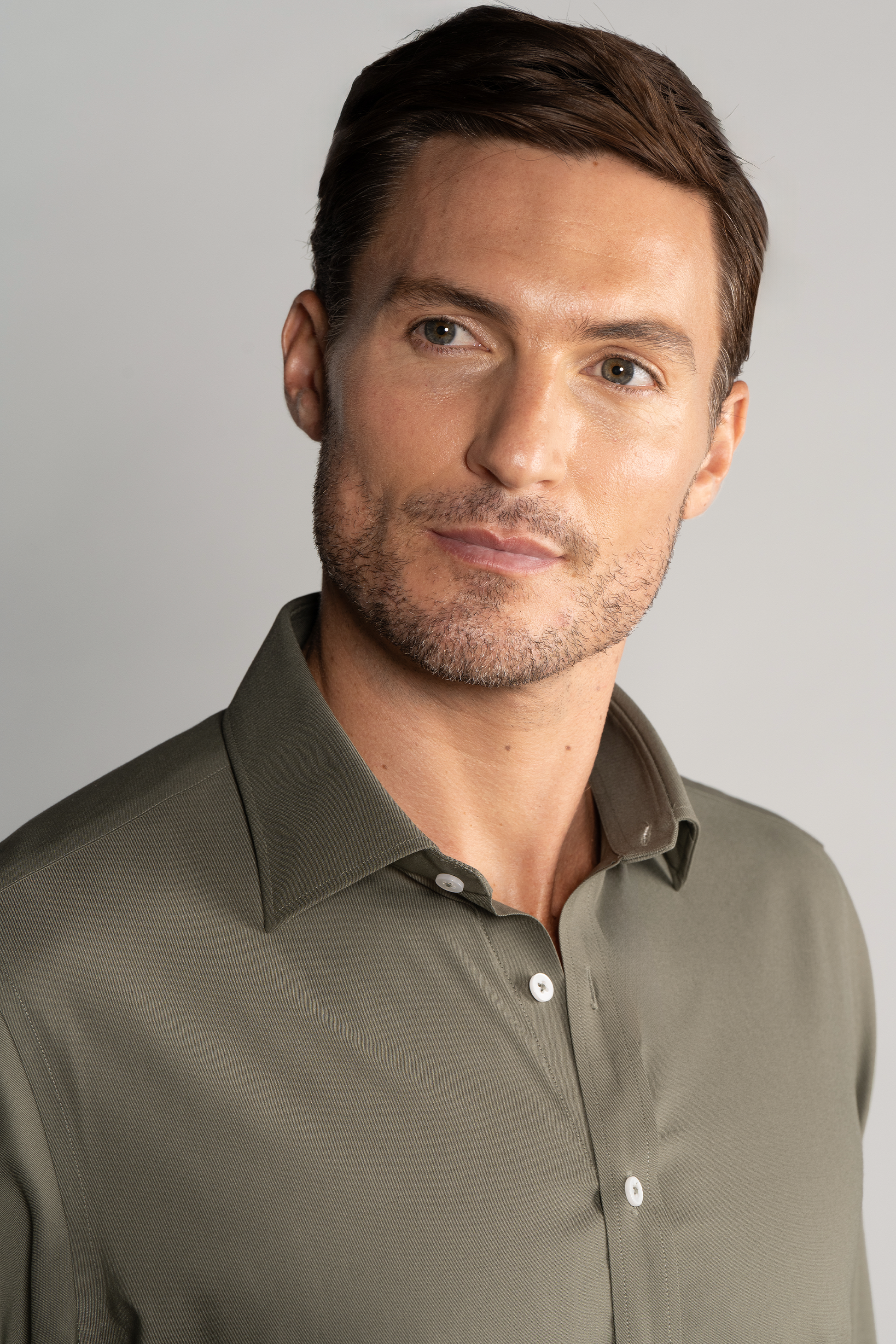 A man with short brown hair and light stubble wears Twillory’s Leader Solid // Olive performance shirt, featuring 4-way stretch. He faces slightly right with a neutral expression against a plain light gray background.