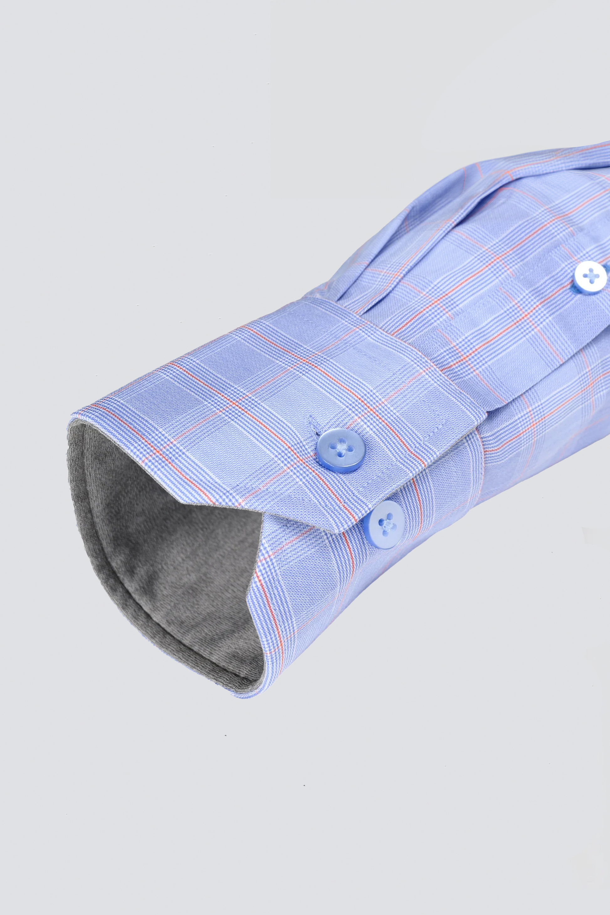 A close-up of Twillory's Leader Plaid // Blue Prince of Wales Performance Shirt sleeve highlights red and white lines, neatly folded cuff with two blue buttons, soft gray inner lining, and moisture-wicking fabric against a light gray background.
