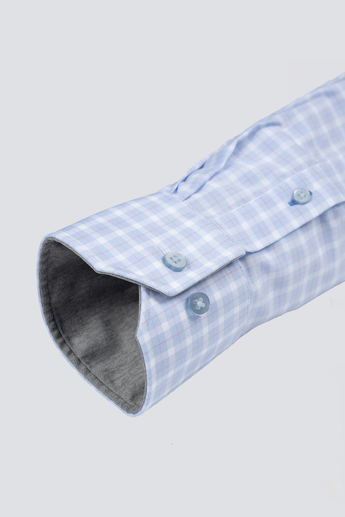 A close-up of the Twillory Leader Plaid // Sky Blue Performance Shirt shows its light blue and white checks, buttoned cuff with two blue buttons, gray inner lining, and 4-way stretch fabric against a plain light gray background.