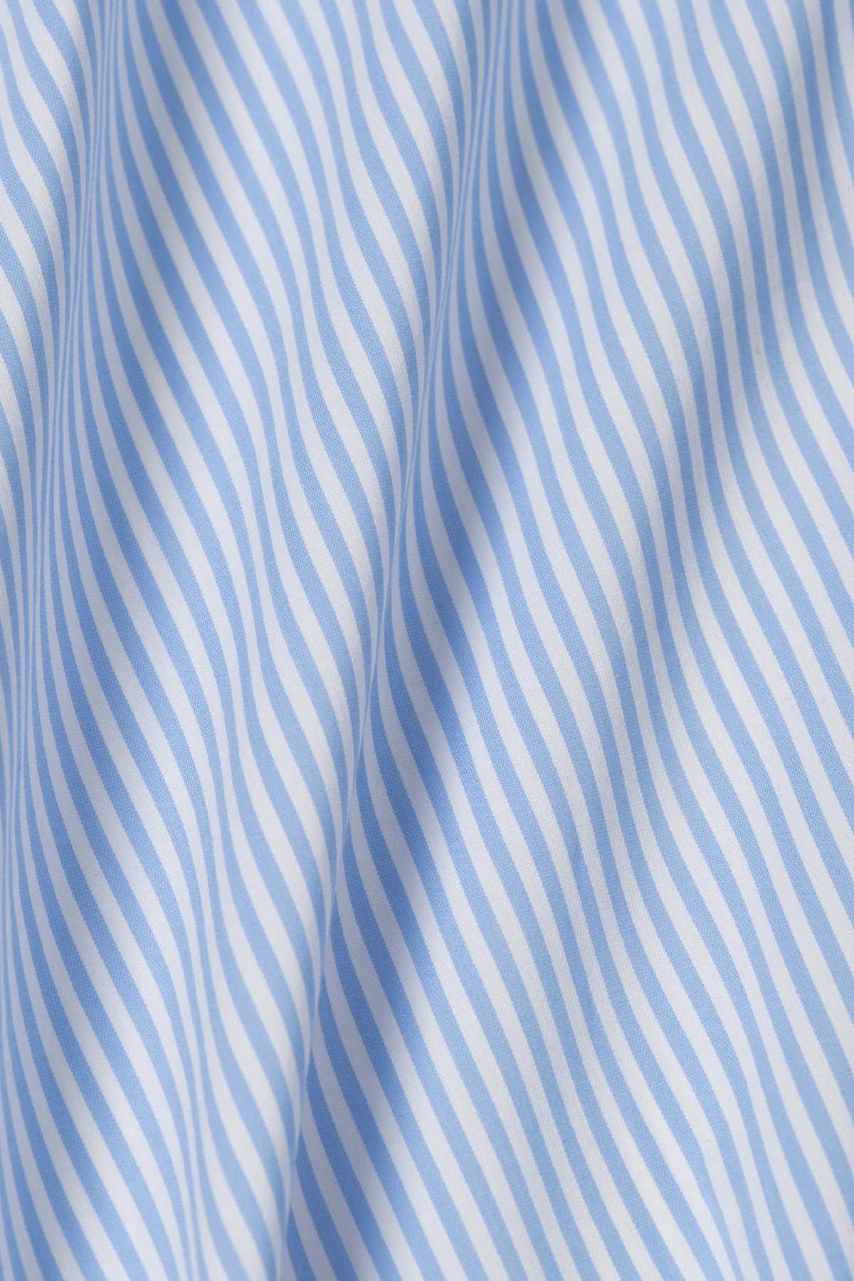 The Leader Stripe // Sky by Twillory features light blue and white vertical stripes on a textured 4-way stretch, moisture-wicking fabric, creating a clean, crisp look with gentle folds and soft shadows.