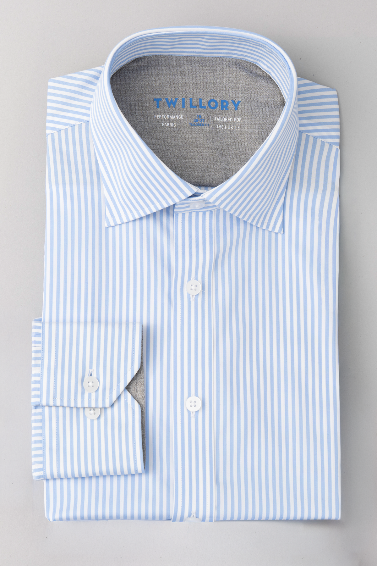 The Twillory Leader Stripe // Sky men’s Performance Shirt features light blue and white vertical stripes, gray inner collar and cuff lining, and a blue Twillory label on a plain background. Front and cuffs are neatly buttoned.