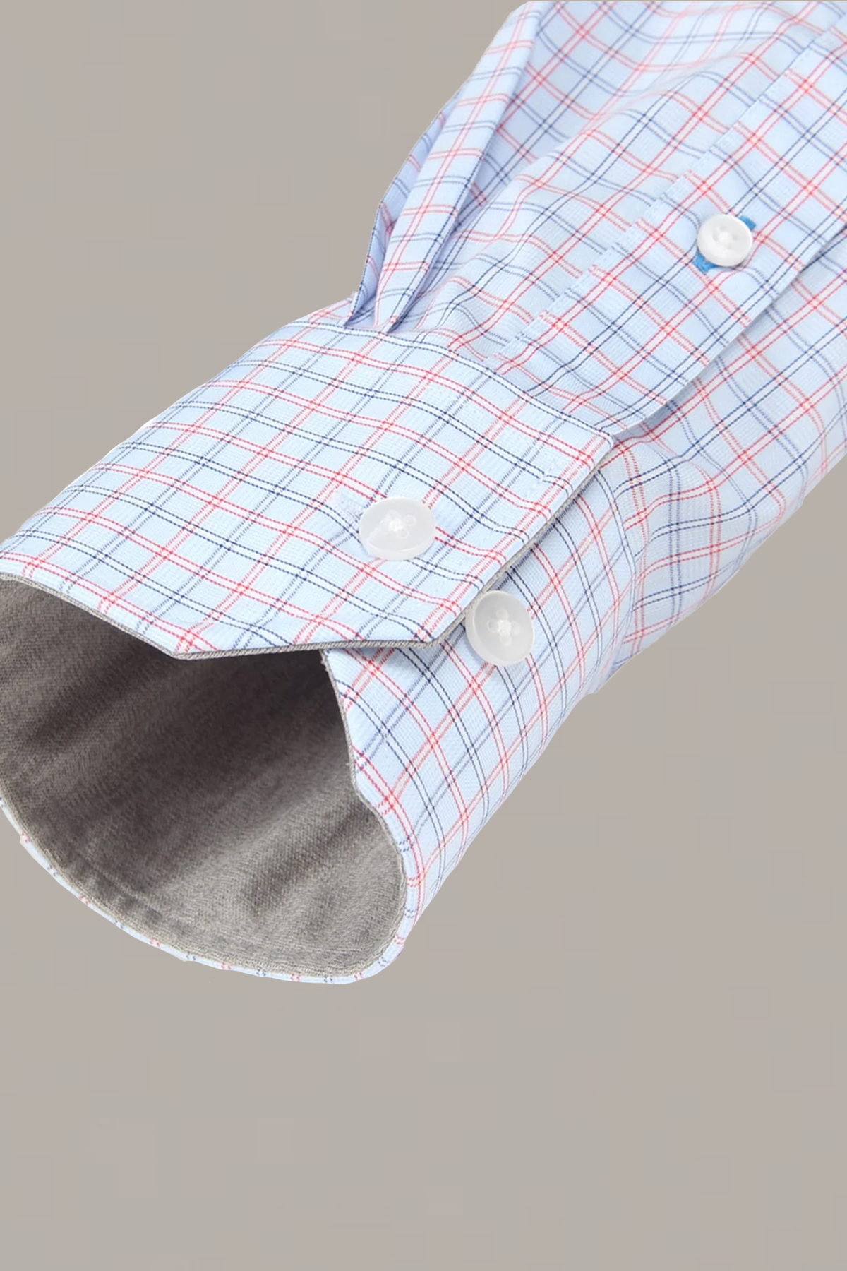 Close-up of Twillory's Leader Windowpane // Red Blue shirt sleeve in light blue, red, and navy plaid. The cuff features two white buttons, a contrasting light gray lining, and moisture-wicking material against a neutral gray background.