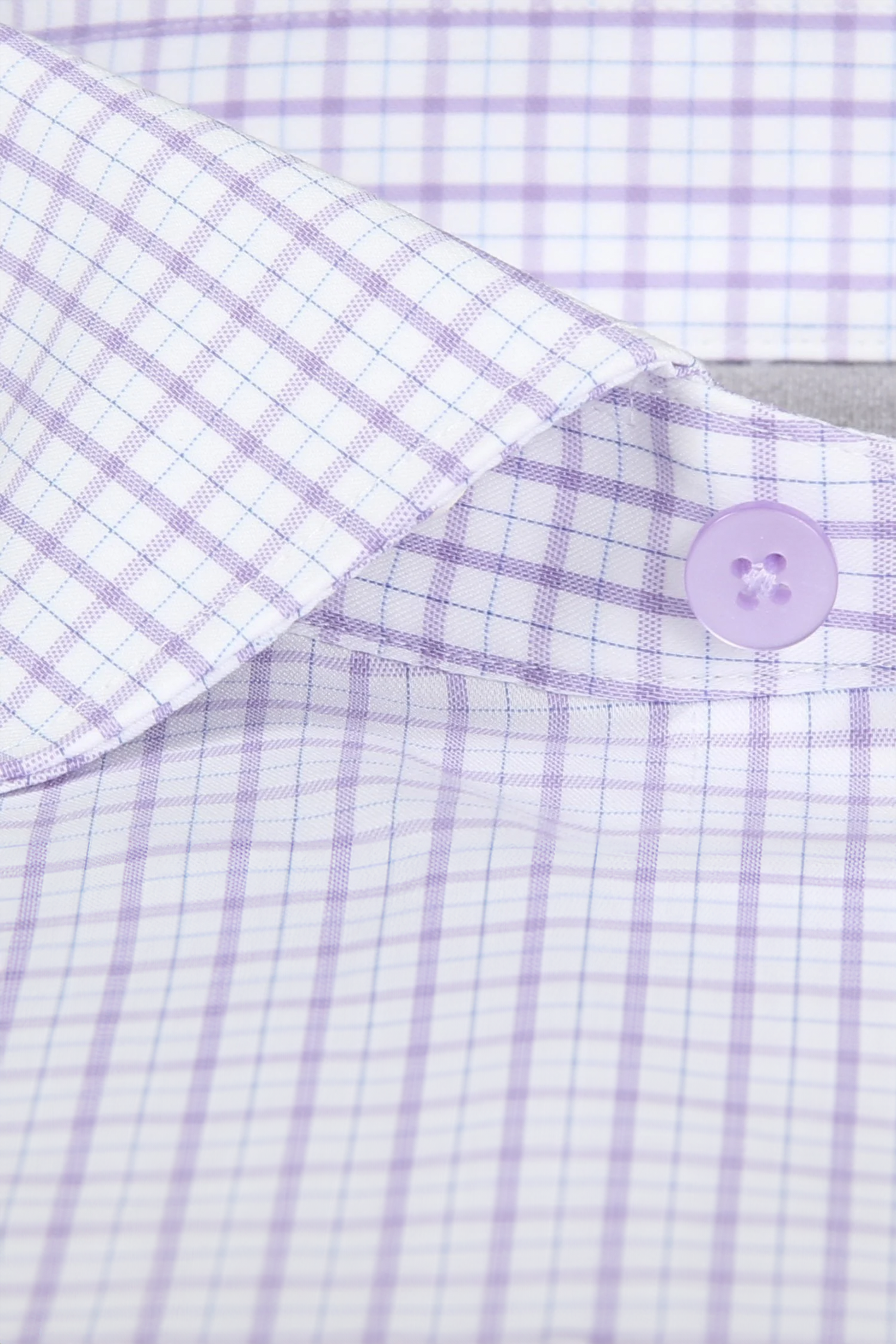Close-up of Twillory's Leader Windowpane // Lavender dress shirt, featuring a light purple and white checkered pattern, purple button, fine blue lines, and smooth 4-way stretch fabric for lightweight all-day comfort.