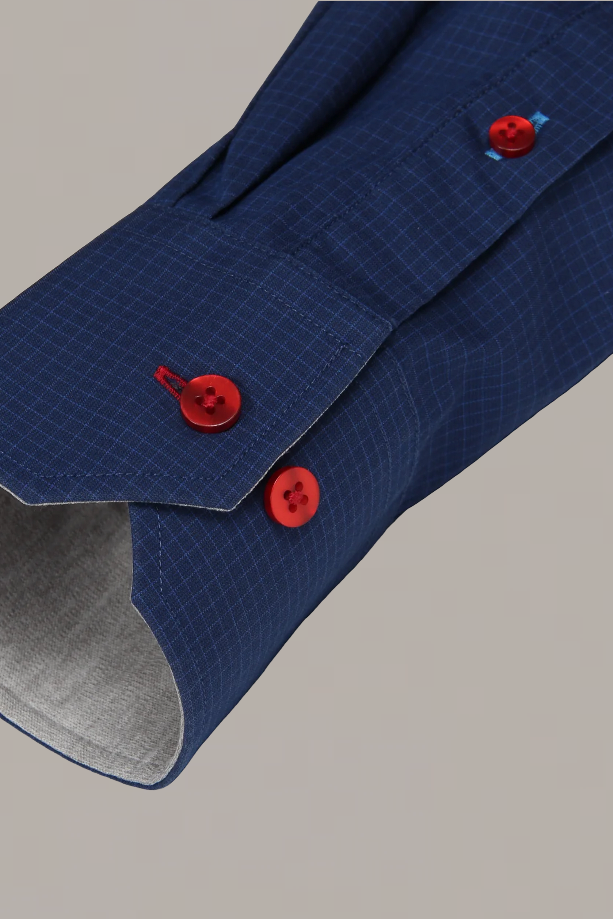 A close-up of Twillory’s Leader Windowpane // Navy Red Contrast shirt sleeve showcases three bold red cuff buttons, a subtle navy grid pattern, and light gray inner lining for a sharp, modern look.