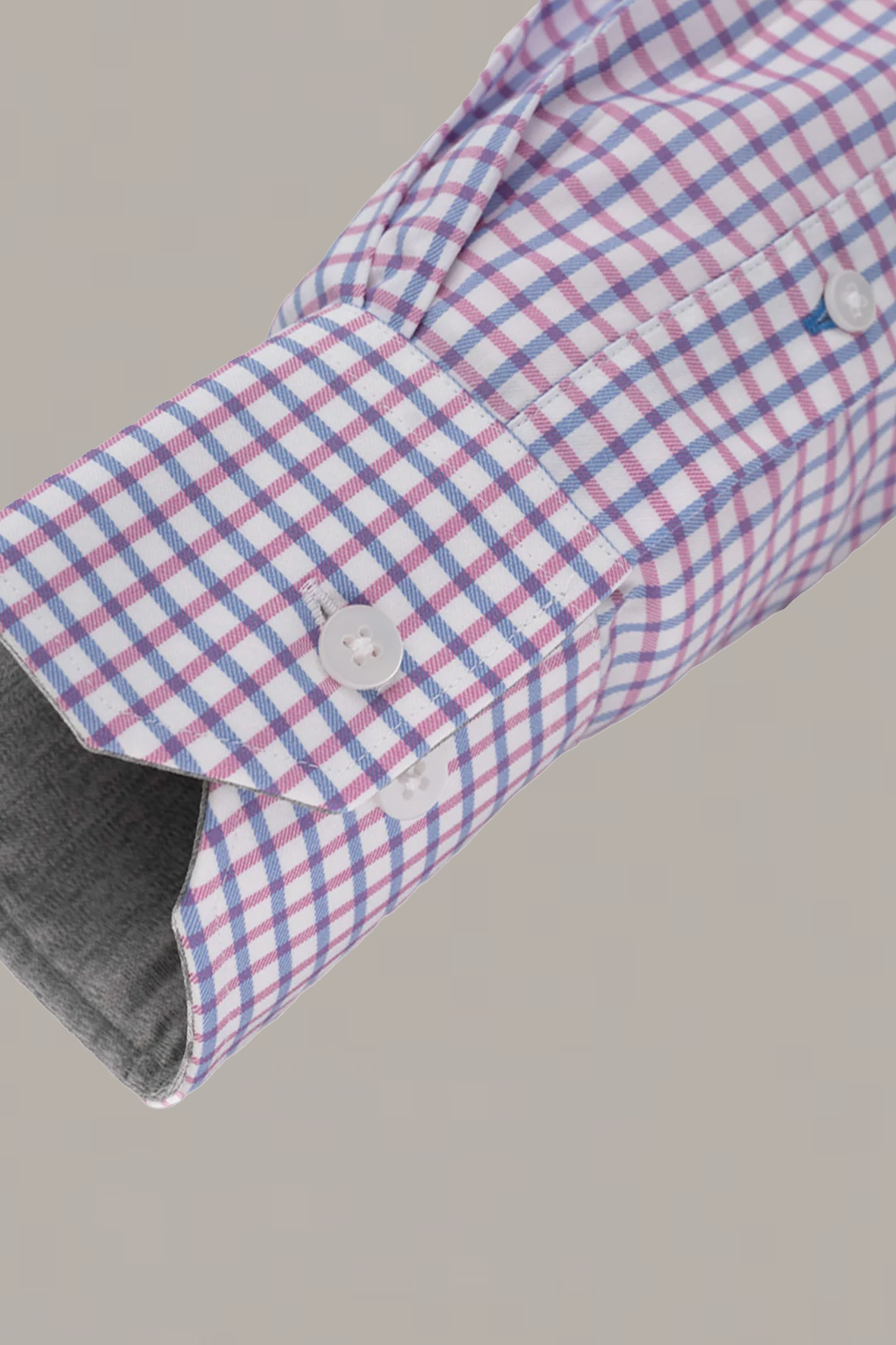 A close-up of Twillory’s Leader Windowpane // Pink Blue performance shirt sleeve shows a pink, blue, and white checkered pattern. The cuff with two white buttons is lined in gray. Moisture wicking and 4-way stretch offer comfort.