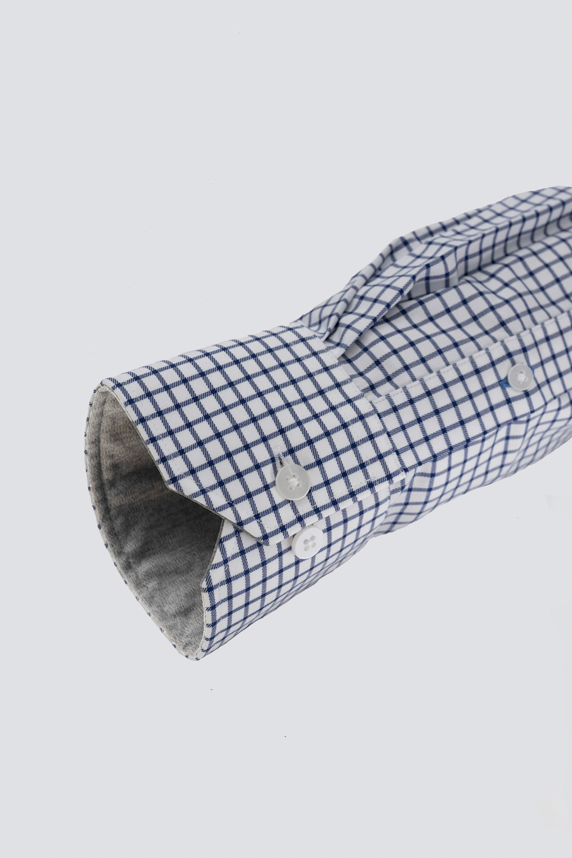 A close-up of the Twillory Leader Windowpane // Navy shirt sleeve, neatly folded to show its blue and white checkered pattern, grey inner lining, white cuff buttons, and 4-way stretch fabric against a plain white background.