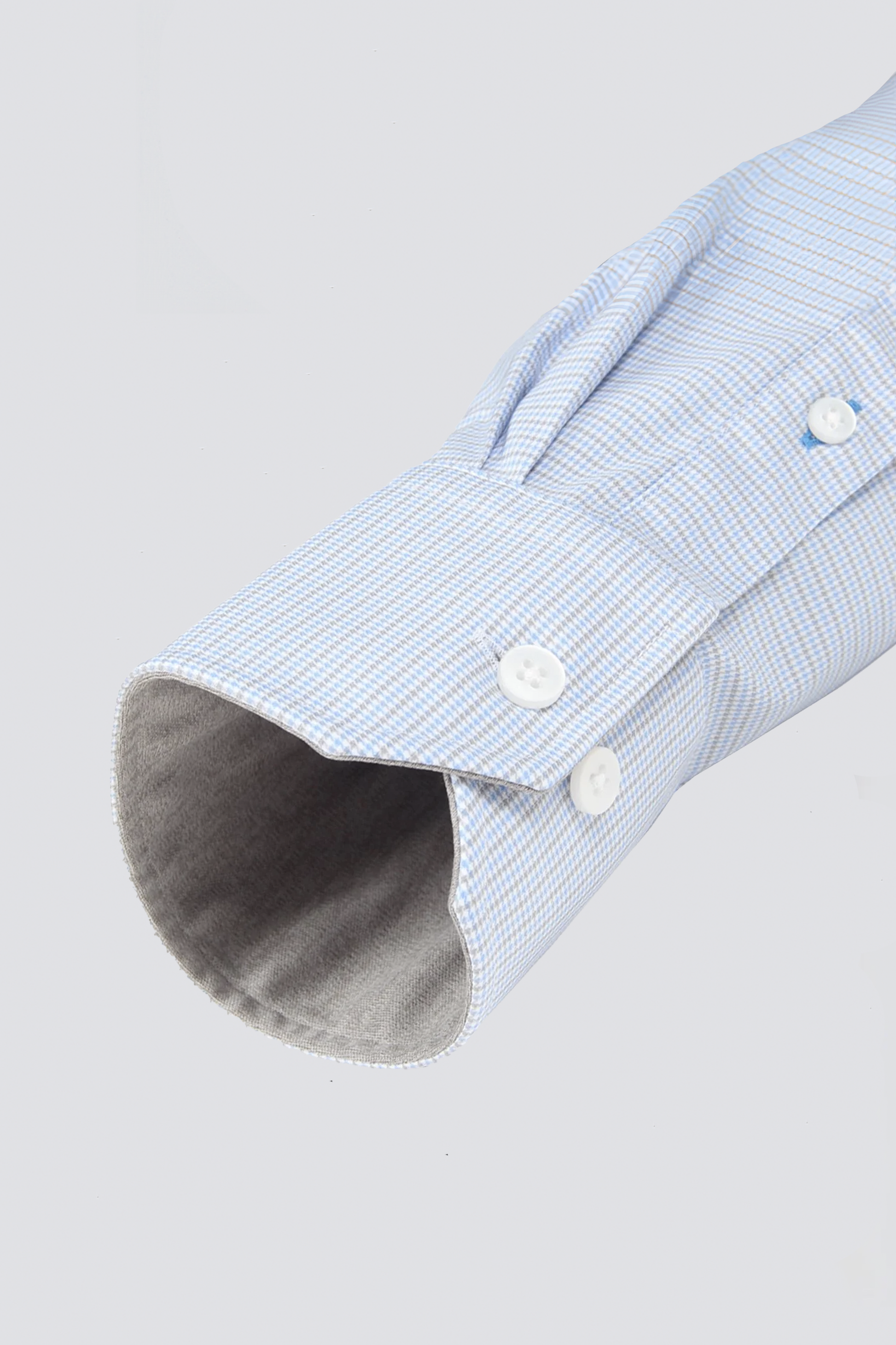 A close-up of Twillory's Leader Houndstooth // Grey Blue shirt cuff, showing a light blue and white houndstooth pattern with two white cuff buttons and one on the sleeve placket. The cuff interior and background are light gray.