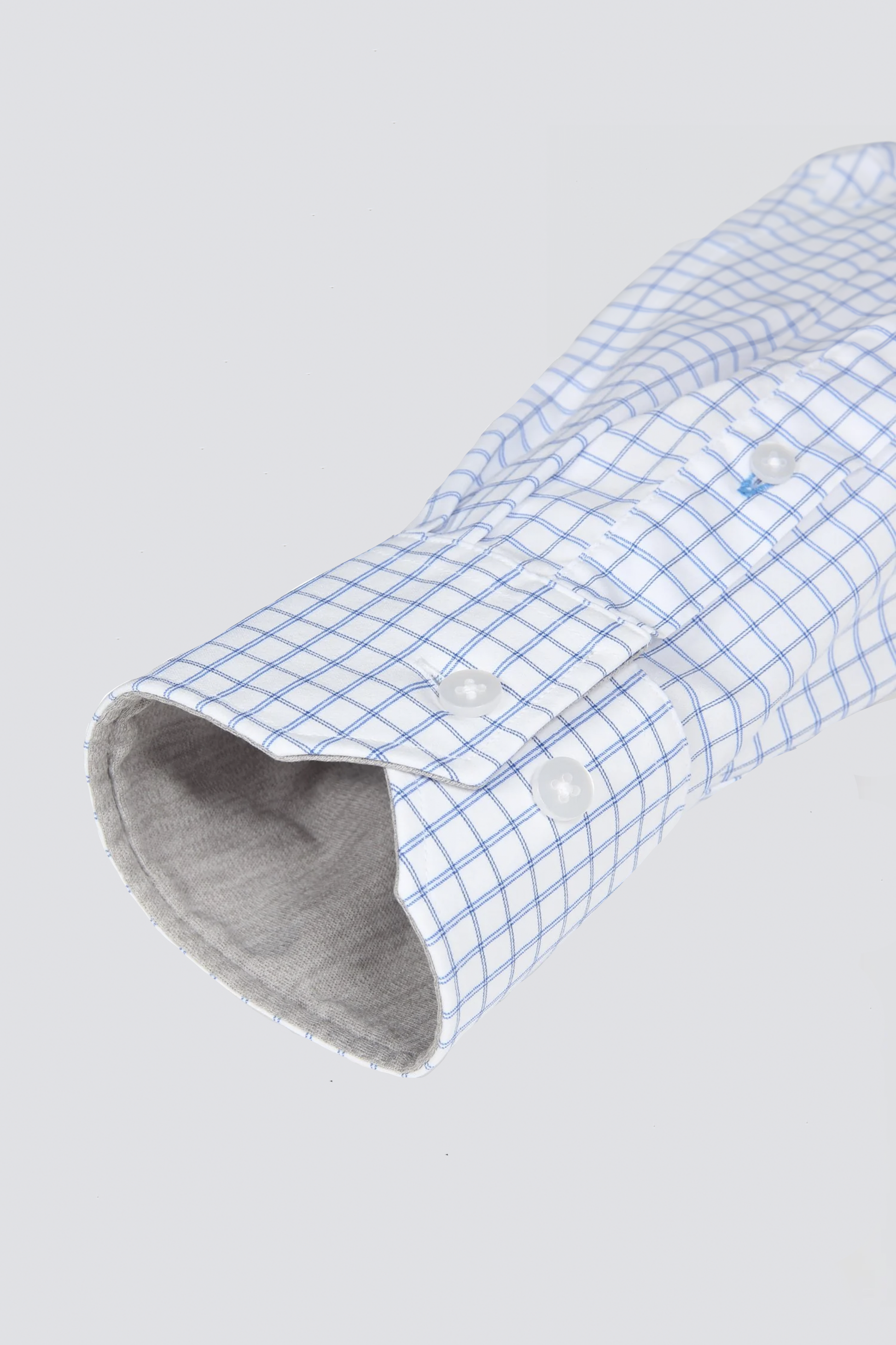 A close-up of the Leader Windowpane // Blue Performance Shirt by Twillory shows its white fabric with a blue grid, unbuttoned cuff with two white buttons, light grey inner lining, and 4-Way Stretch comfort against a light grey background.