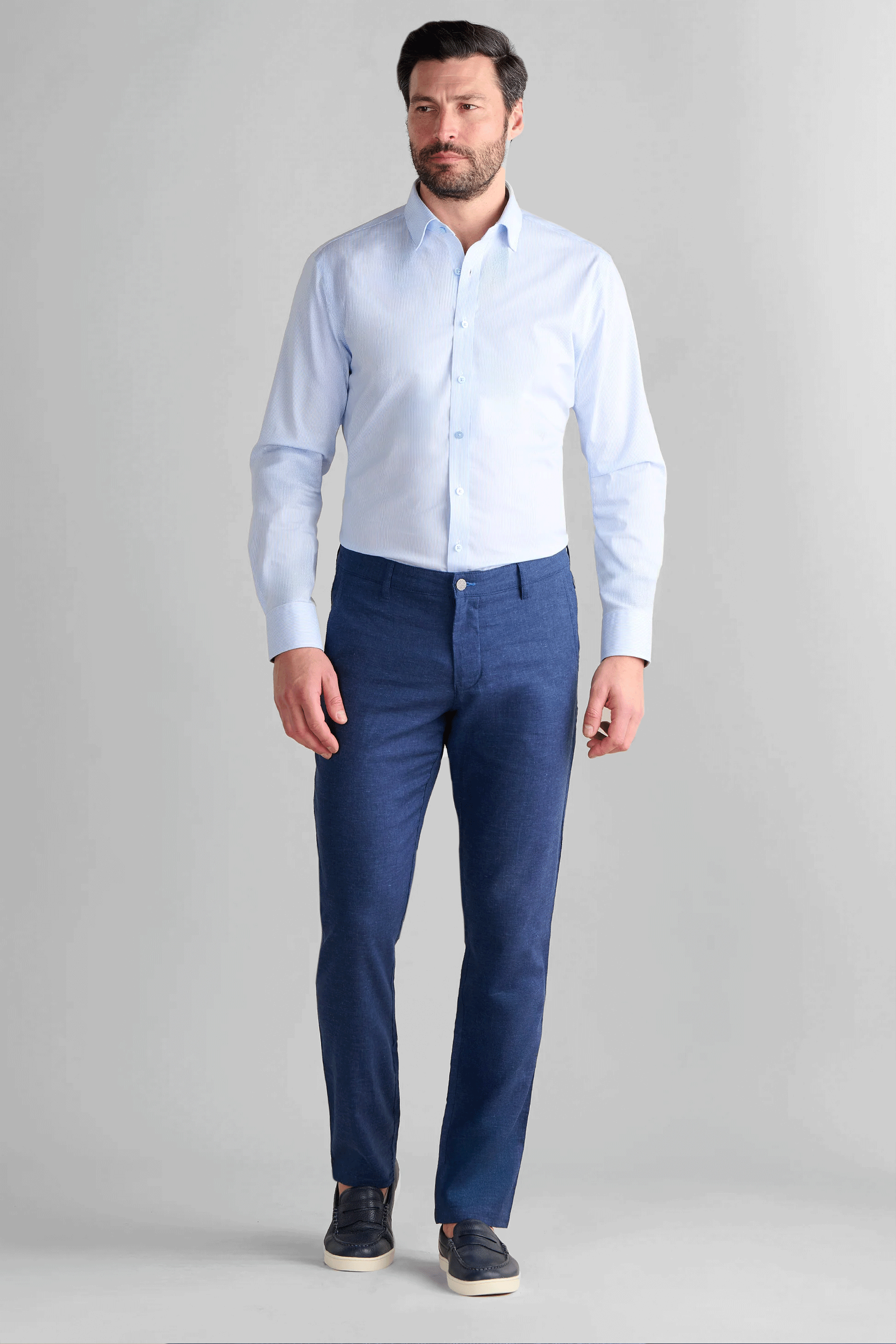 A man wearing Twillory Performance Linen Pants in Blue, featuring a tailored fit and breathable, wrinkle-resistant fabric. The outfit is styled with a light blue button-down shirt and navy leather loafers, highlighting the pants' non-iron texture and professional casual look.