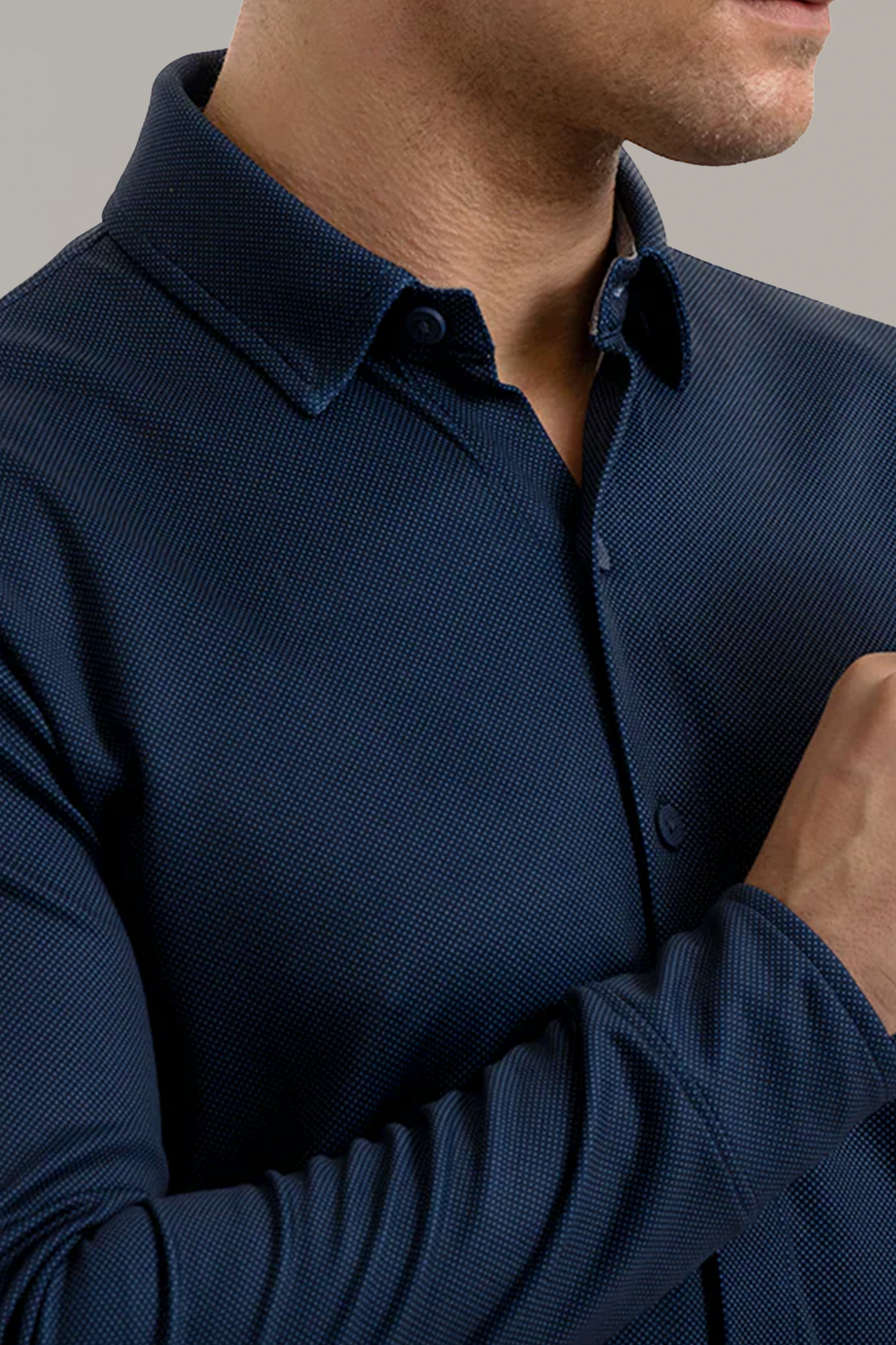 A man is shown from the nose down, wearing Twillory’s Long Sleeve Button Down Polo Dot in Navy. The shirt features a pointed collar, buttoned cuffs, and subtle polo dot texture. His right hand is raised near his chin.