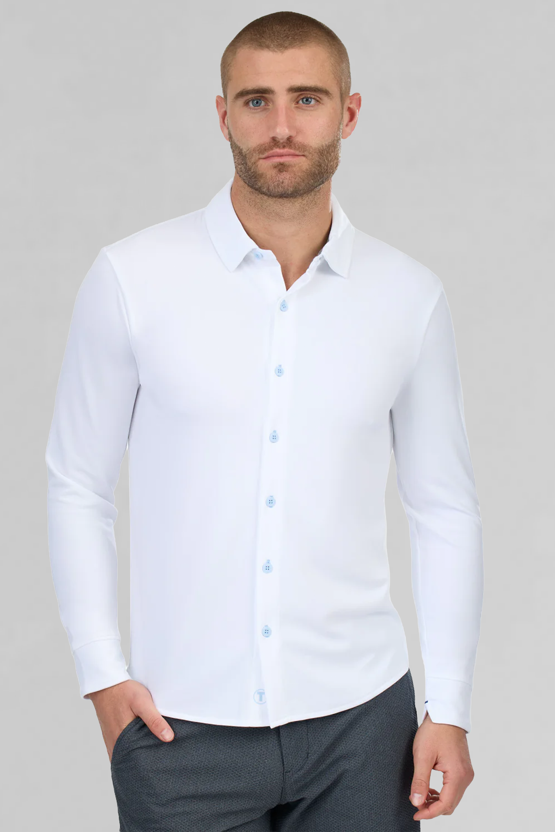 A man with close-cropped hair and a trimmed beard wears the Twillory Long Sleeve Button Down Polo Contrast in Powder Blue White, paired with dark gray pants and posed against a plain light gray background.