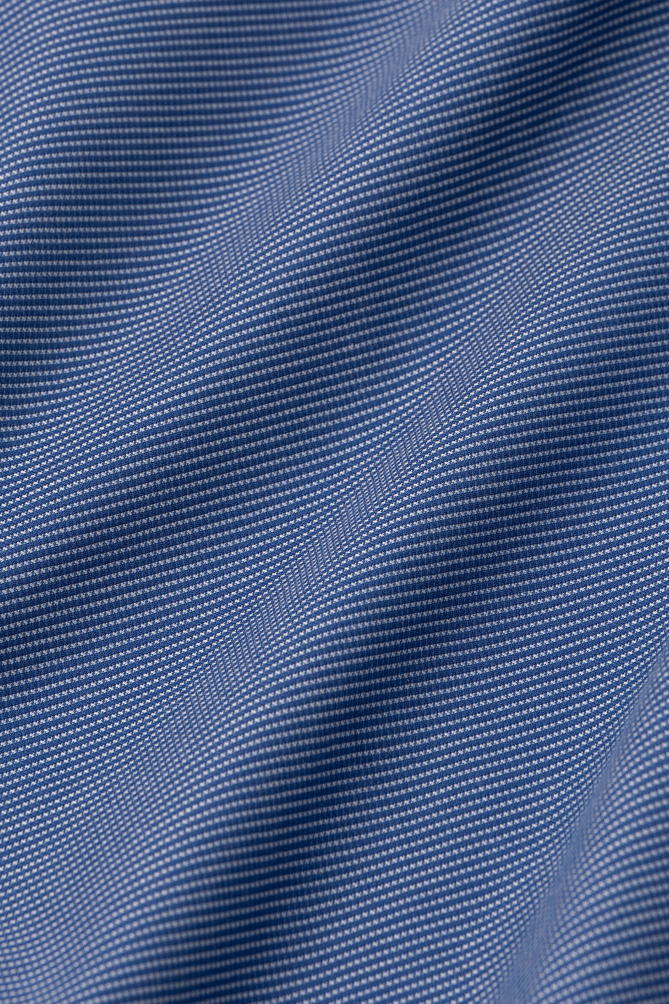 Close-up of Twillory's Non-Iron Twilight Pin Dot shirt shows blue fabric with a fine grid pattern. Soft waves and folds highlight the smooth, slightly reflective, hyper-breathable texture and weave.