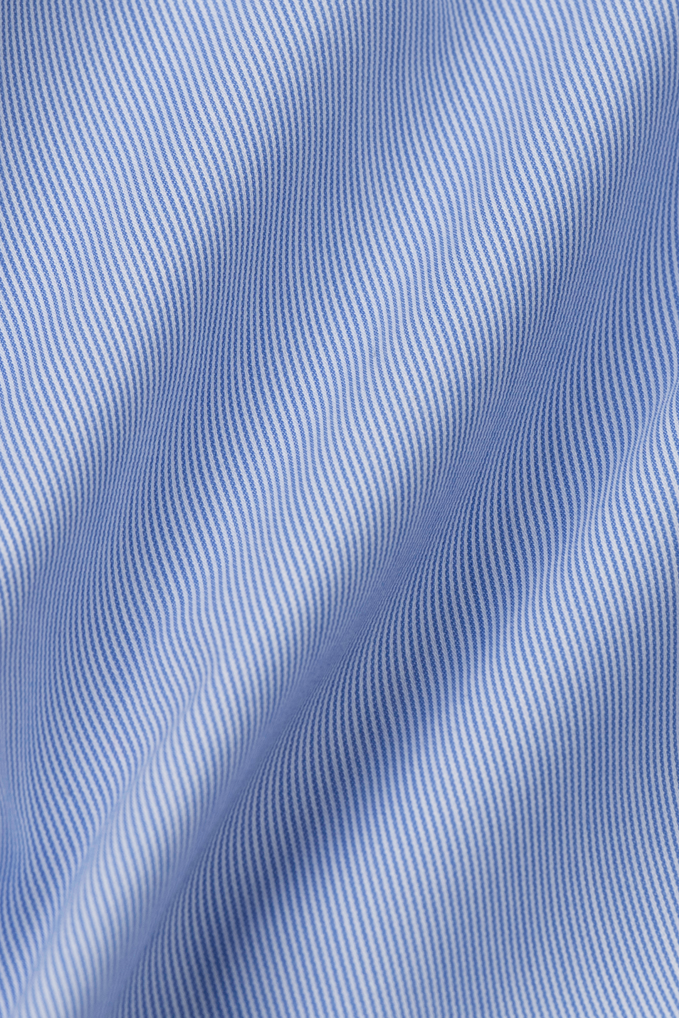Close-up of Twillory's Leader Stripe // Micro Blue shirt fabric shows evenly spaced blue and white pinstripes on 4-way stretch material, forming soft folds and gentle waves for added texture. Stripes are parallel with fine vertical detailing.