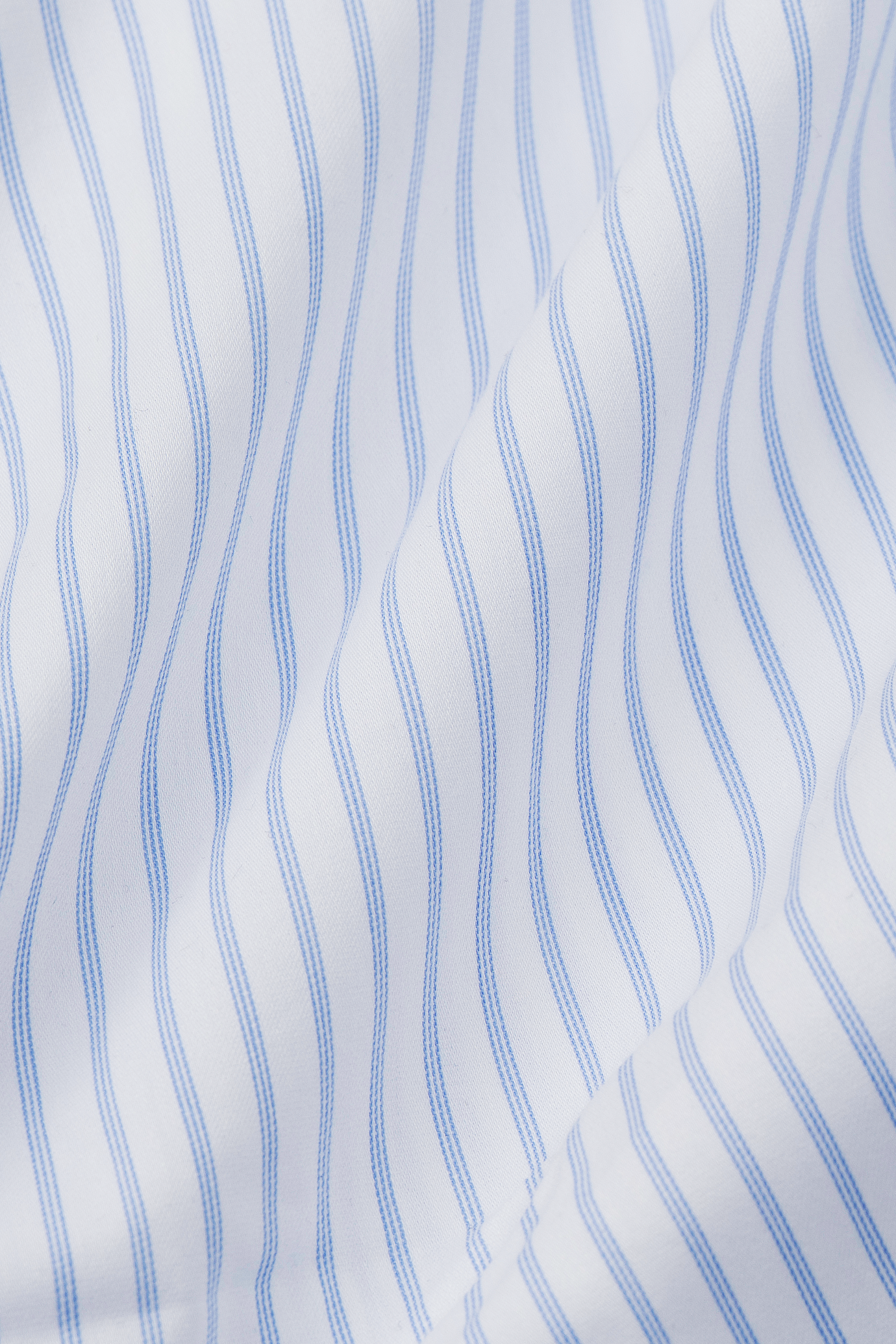A close-up of Twillory’s Leader Stripe // Thick White shows white fabric with bold, evenly spaced blue stripes. Slightly wrinkled for soft shadows, this Performance Shirt offers 4-Way Stretch for comfort and style.
