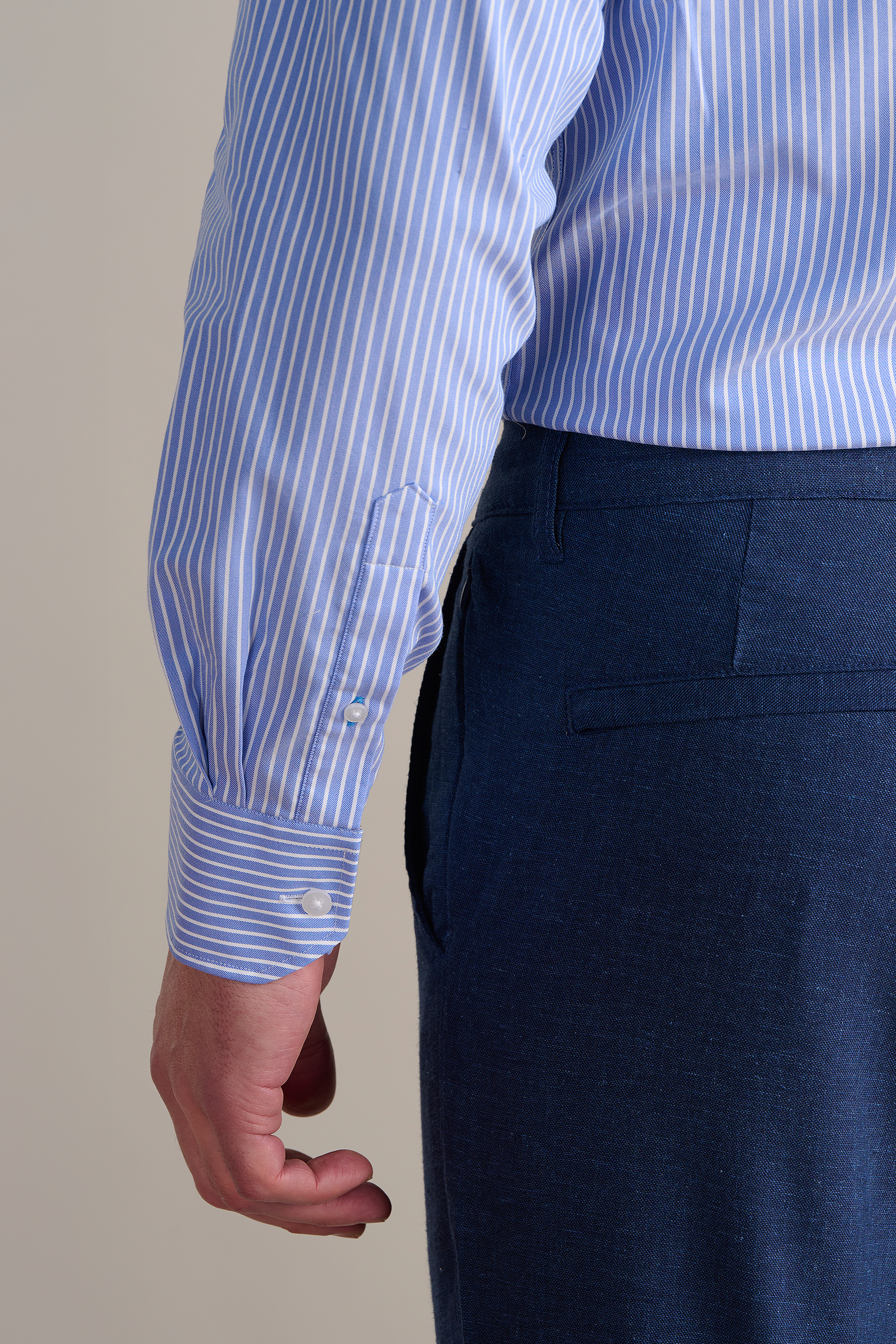 A person wears Twillory’s Leader Stripe // Mini Blue Performance Shirt and dark blue tailored trousers, shown from the back and side. The shirt has white cuff buttons and 4-way stretch fabric; the trousers feature a back pocket.