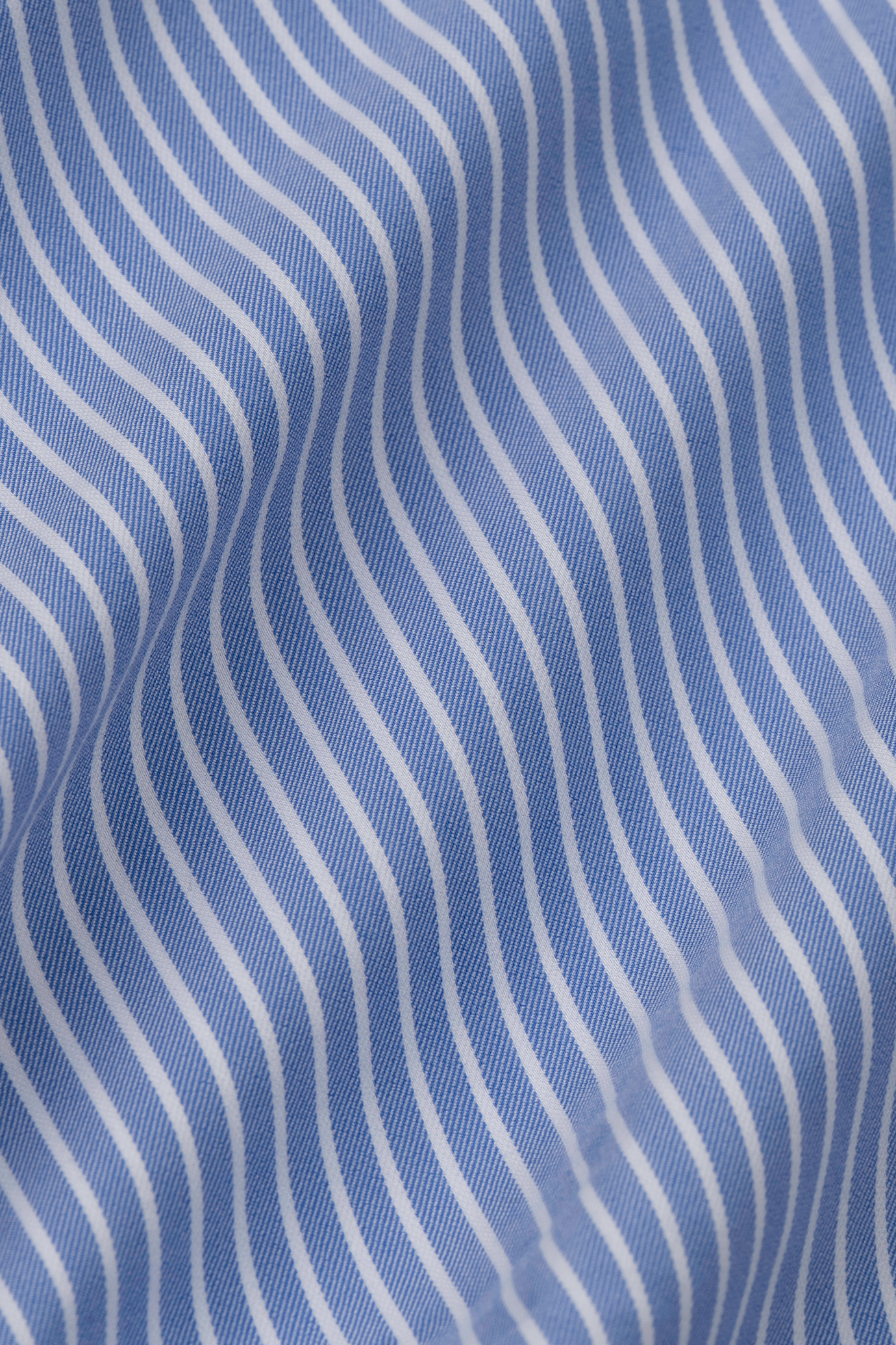 Close-up of Twillory’s Leader Stripe // Mini Blue shirt fabric. The blue and white stripes form a wavy, dynamic pattern on soft, slightly reflective 4-way stretch material with moisture-wicking properties.