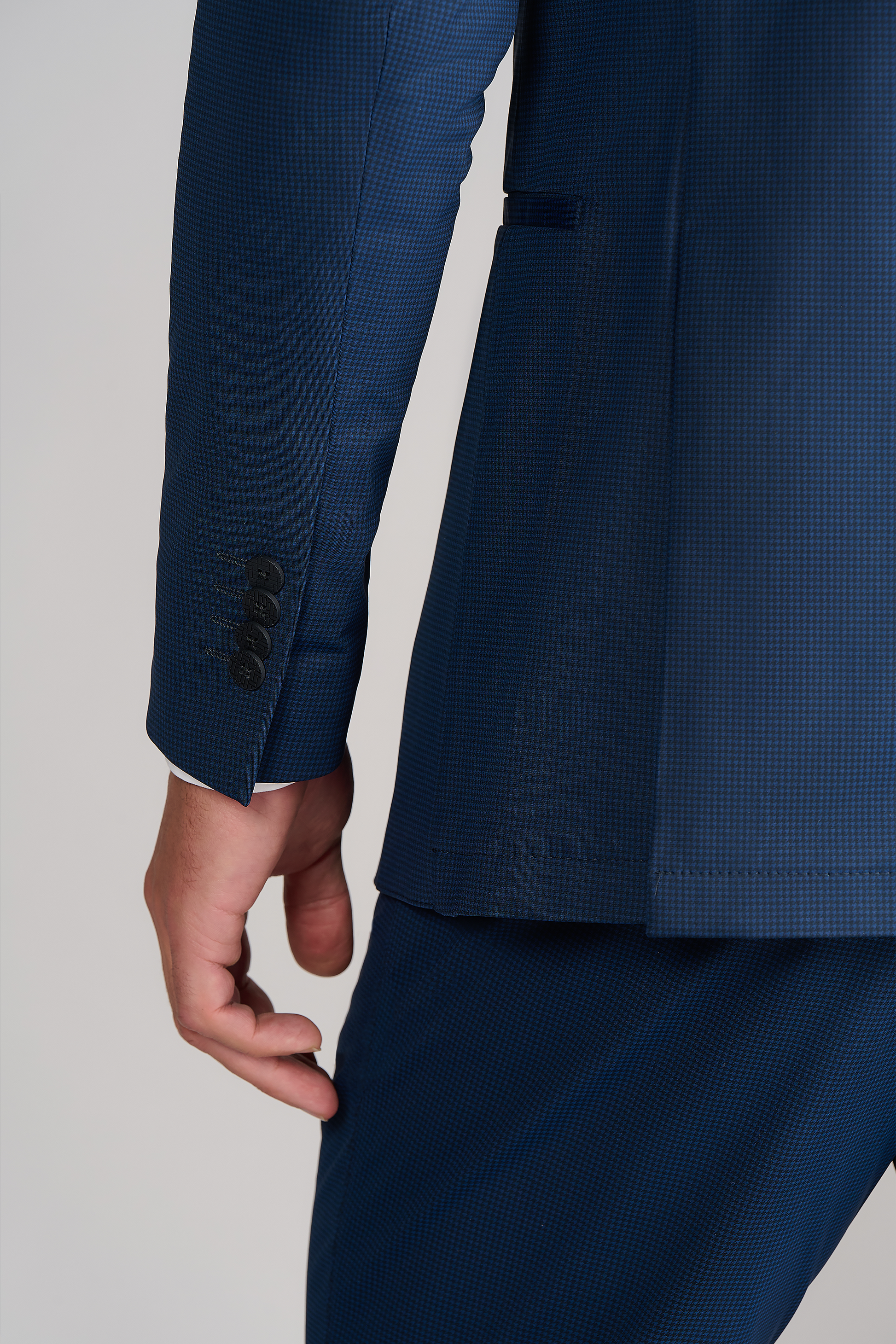 A close-up shows a person in the Twillory Performance Blazer // Navy Houndstooth, focusing on their left arm and hand with the cuff's three black buttons and part of the pocket against a plain, light background.