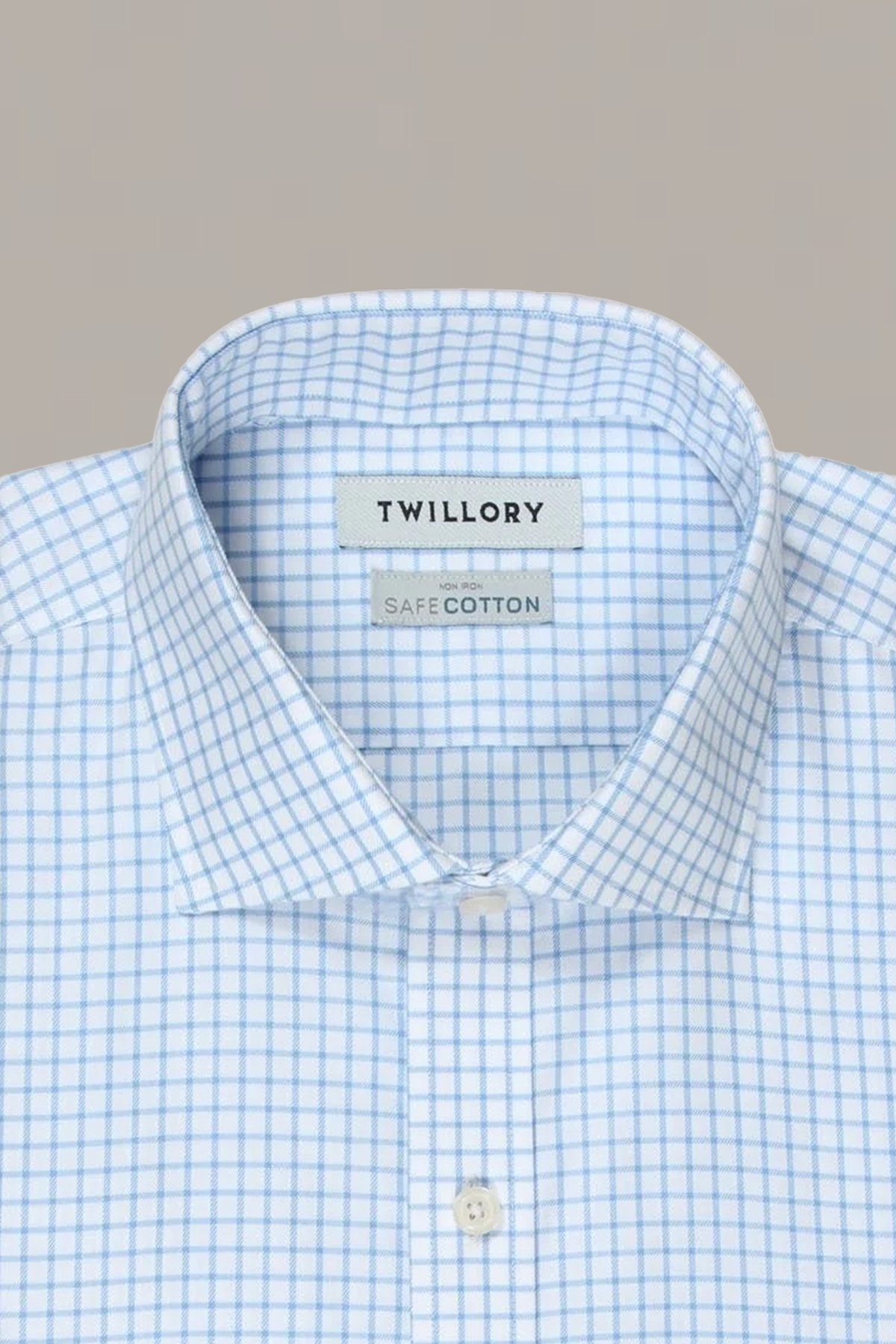 A close-up of a neatly pressed Twillory Non-Iron Sky Windowpane shirt with light blue and white checks, set against a plain beige background. The label displays the Twillory brand.
