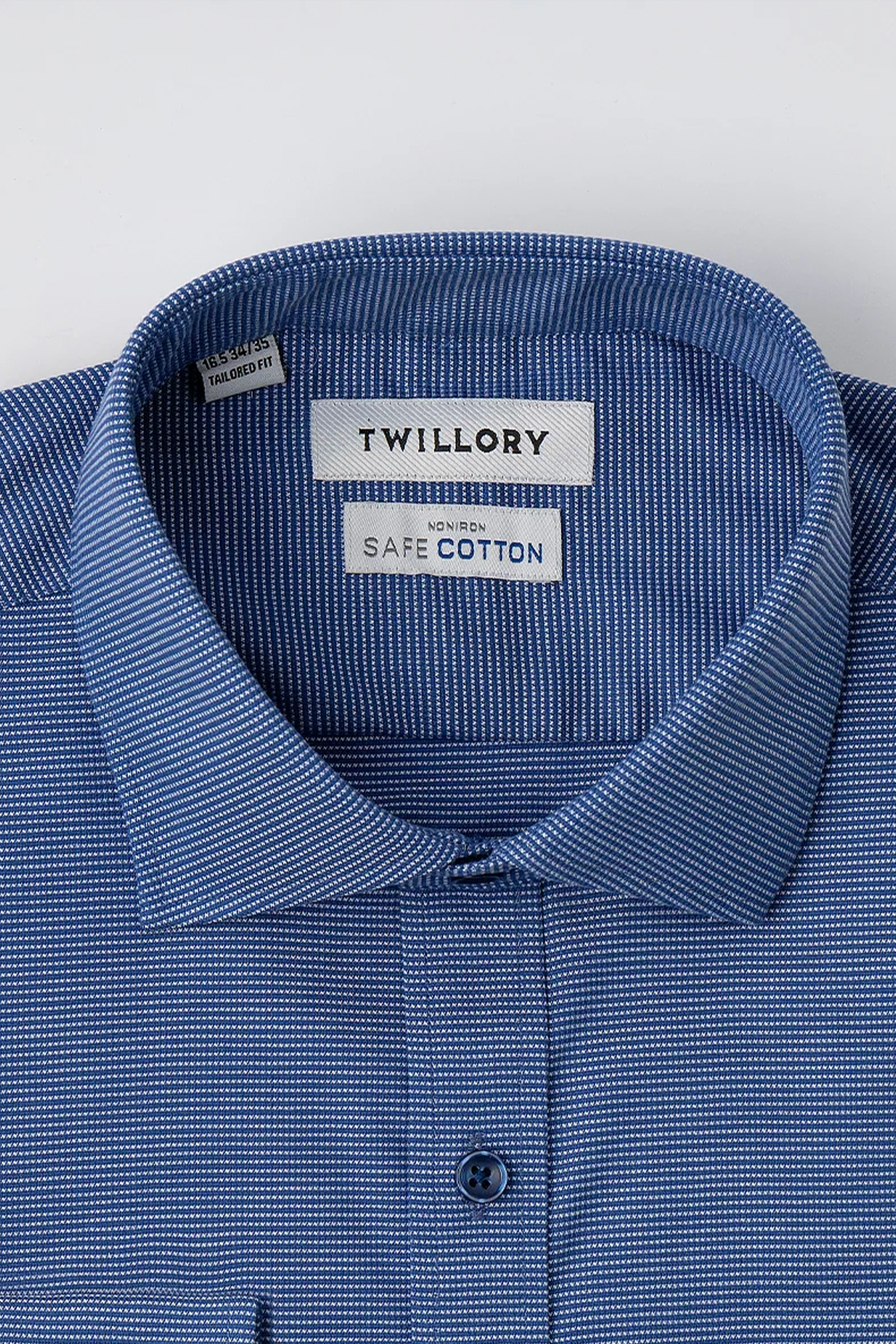 A close-up of Twillory’s Non-Iron Twilight Pin Dot shirt in blue shows the neat collar with “Twillory” and “Non-Iron SafeCotton” labels. The shirt’s subtle white pin dot pattern and fastened top button offer a crisp, hyperbreathable look.