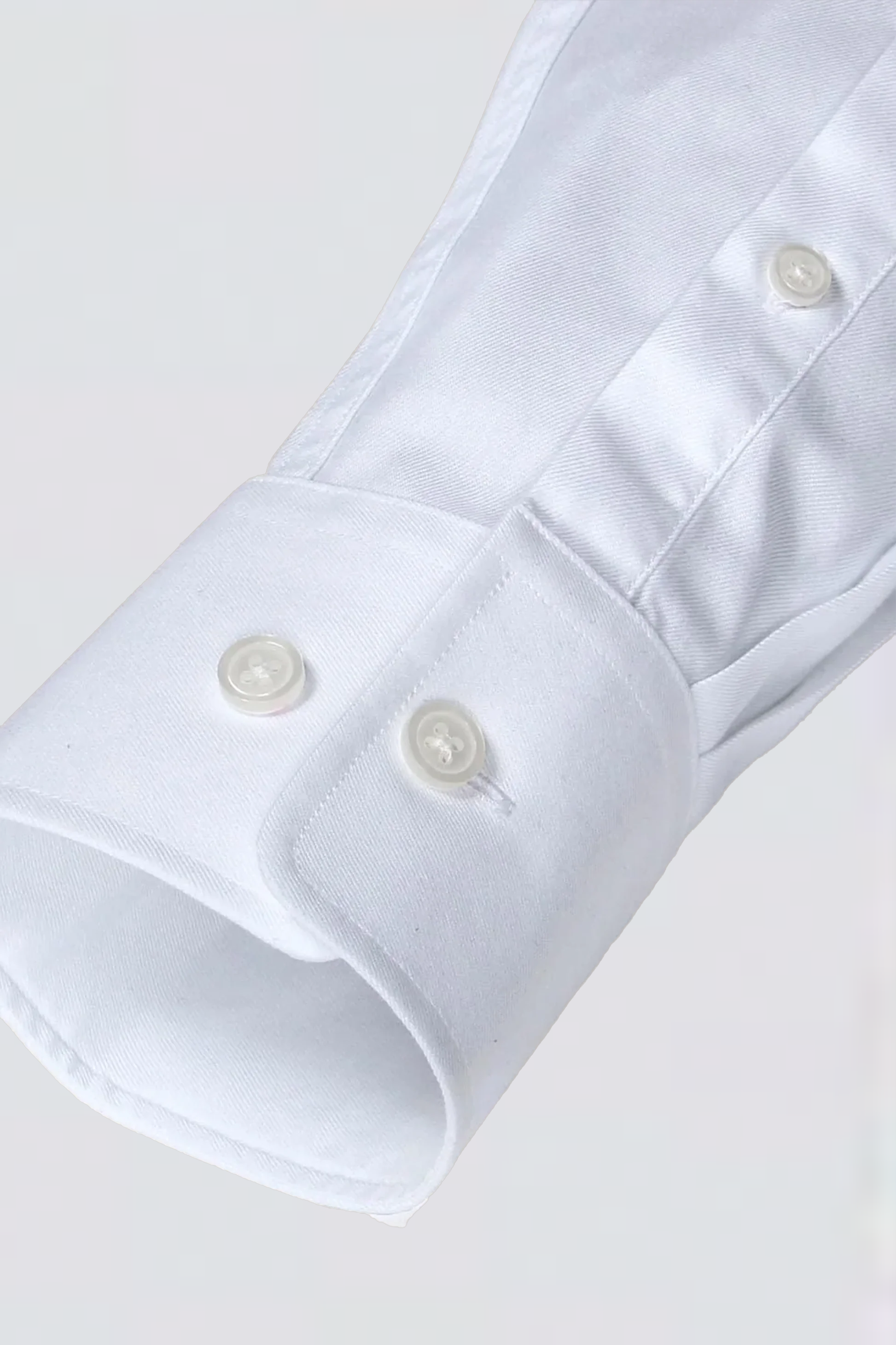 A close-up of the Twillory Non-Iron White Twill shirt sleeve shows a classic cuff with two white buttons and visible stitching. The hyperbreathable, non-iron fabric looks smooth and crisp against a light grey background.
