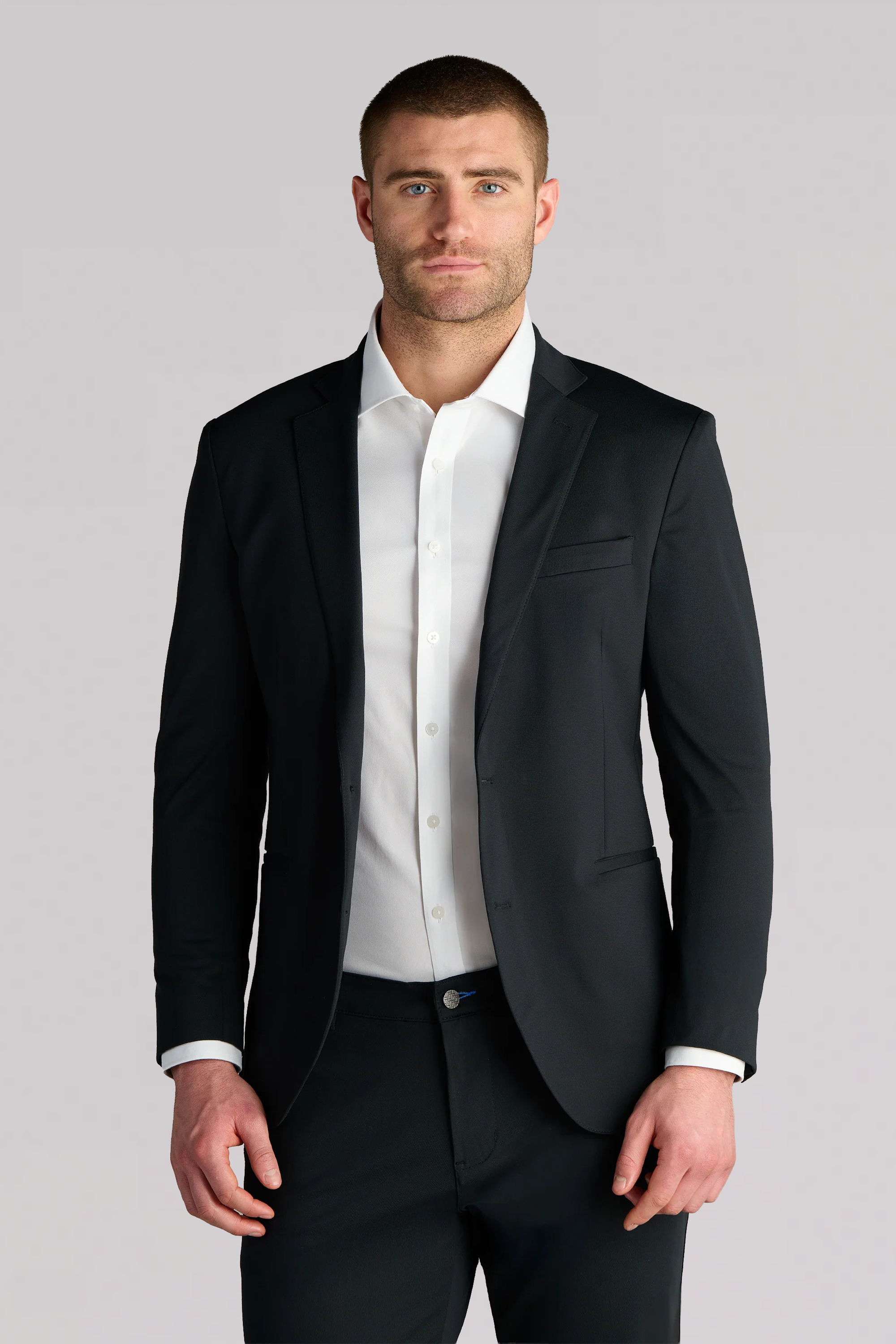 A man wearing the Performance Blazer // Black, a white dress shirt, and black pants stands facing forward against a plain light gray background.
