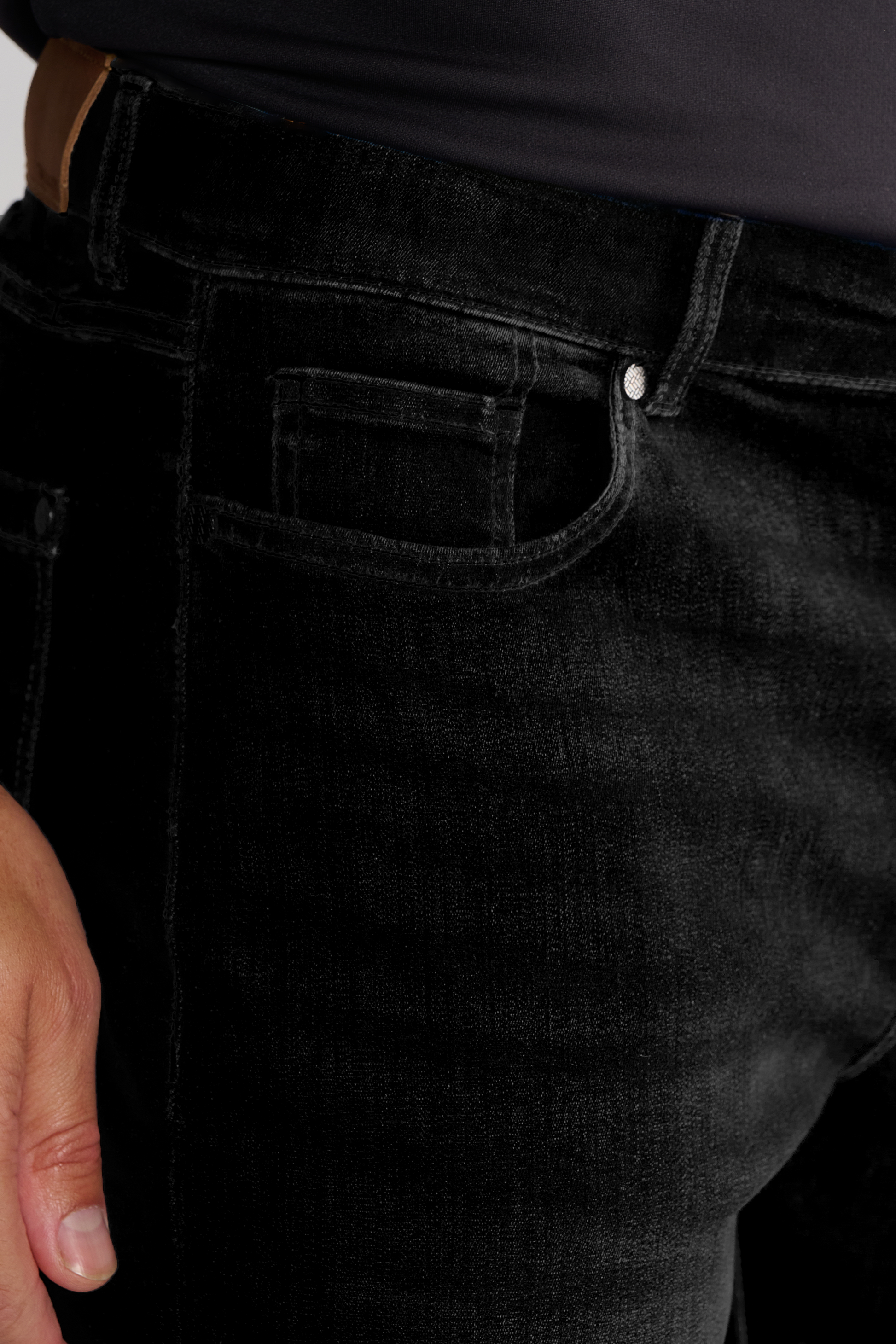 Close-up of a person wearing Twillory's Performance Denim // PURE BLACK jeans with a tapered fit and dark shirt. The image highlights the front pocket, waistband, and belt loop, while their left hand rests by the hip on slightly faded fabric.