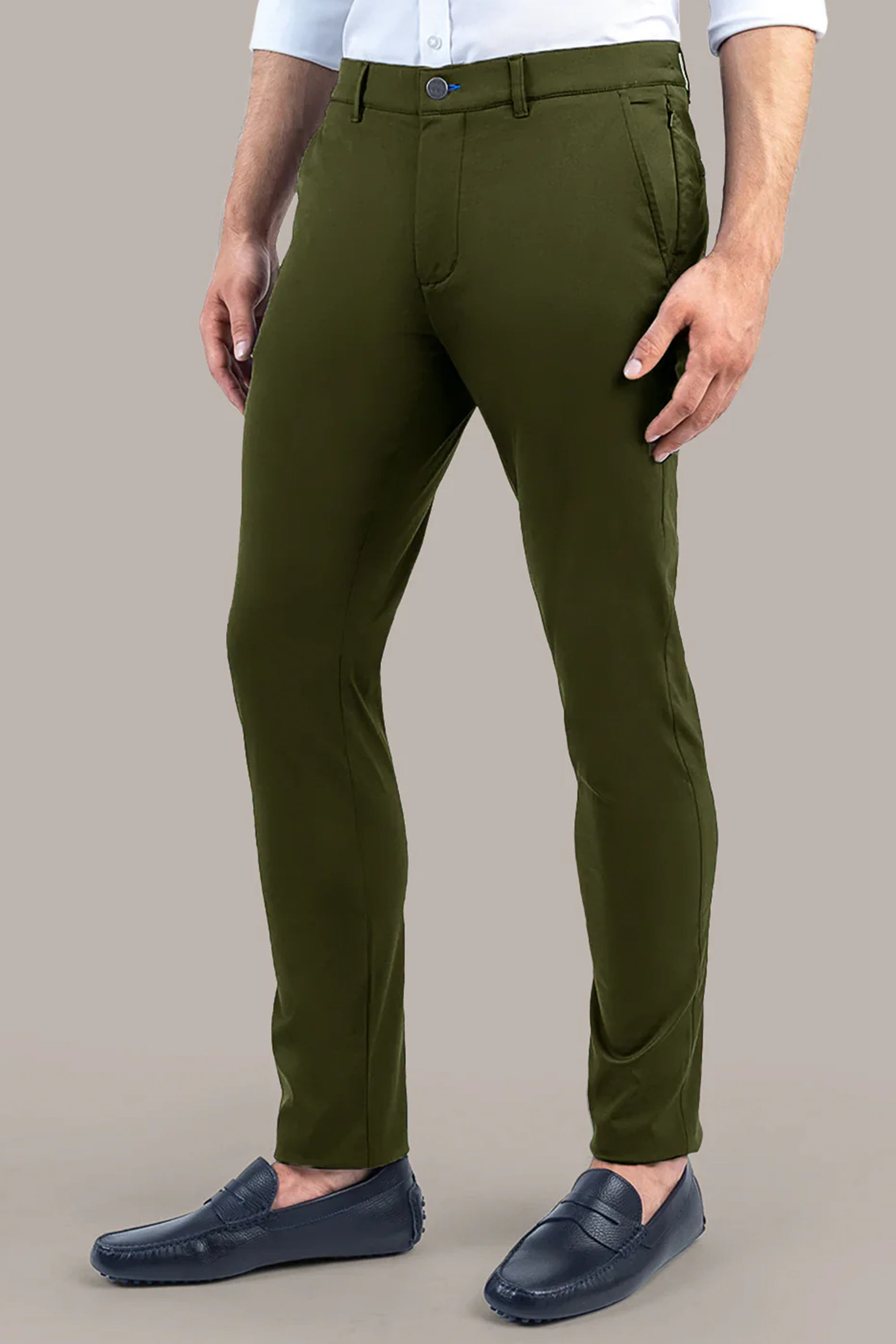 A man wears Twillory Performance Pants // SAGE with front pockets, paired with a white dress shirt and navy loafers. His hands rest by his sides, while the plain light grey background highlights the fit and details of the pants.