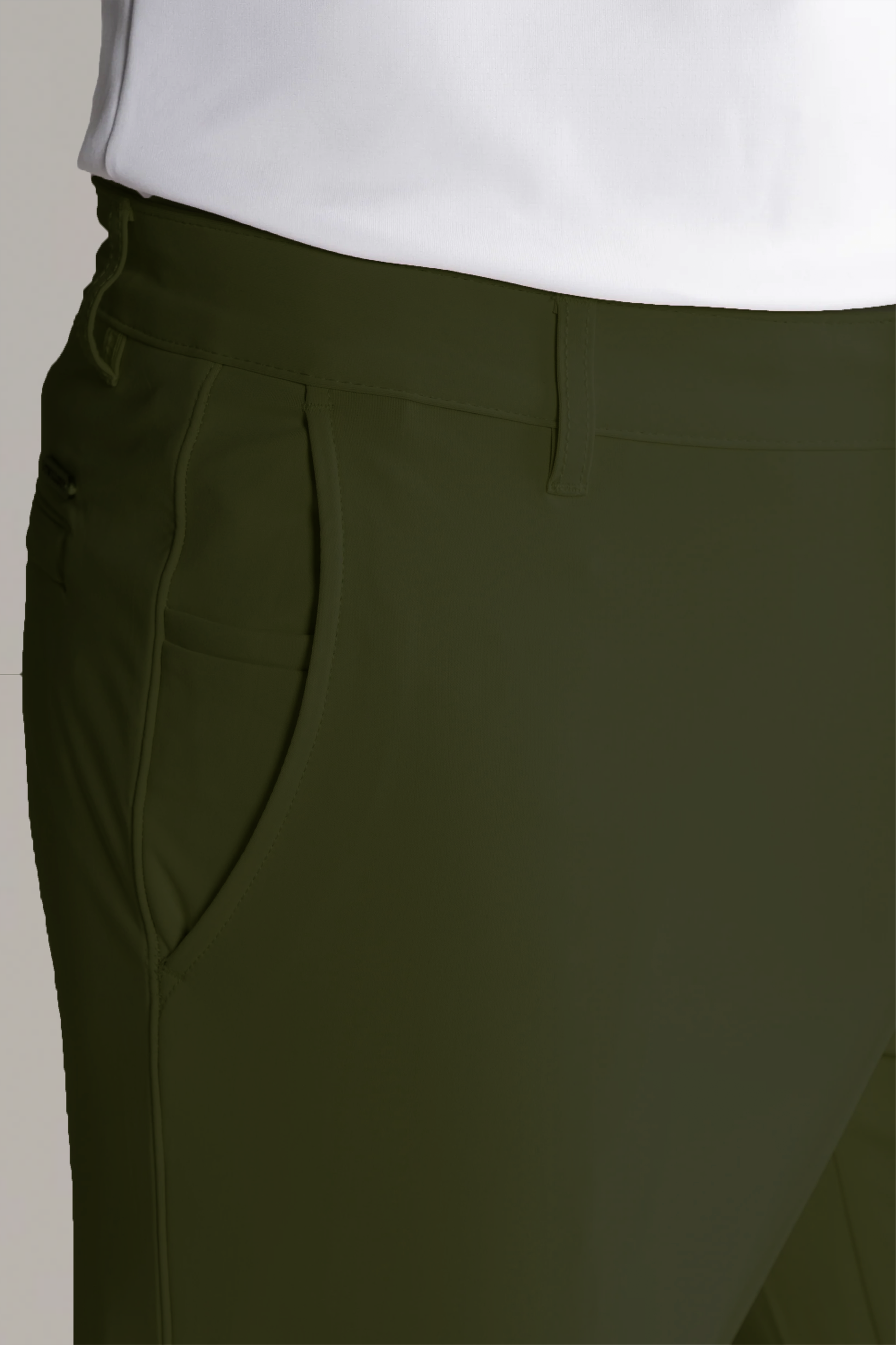 Close-up of a person wearing Twillory Performance Pants // SAGE—dark green non-iron stretch pants with belt loops, front pockets, prominent stitching, and a small side zipper pocket. A white shirt is tucked in; the background is neutral and blurred.