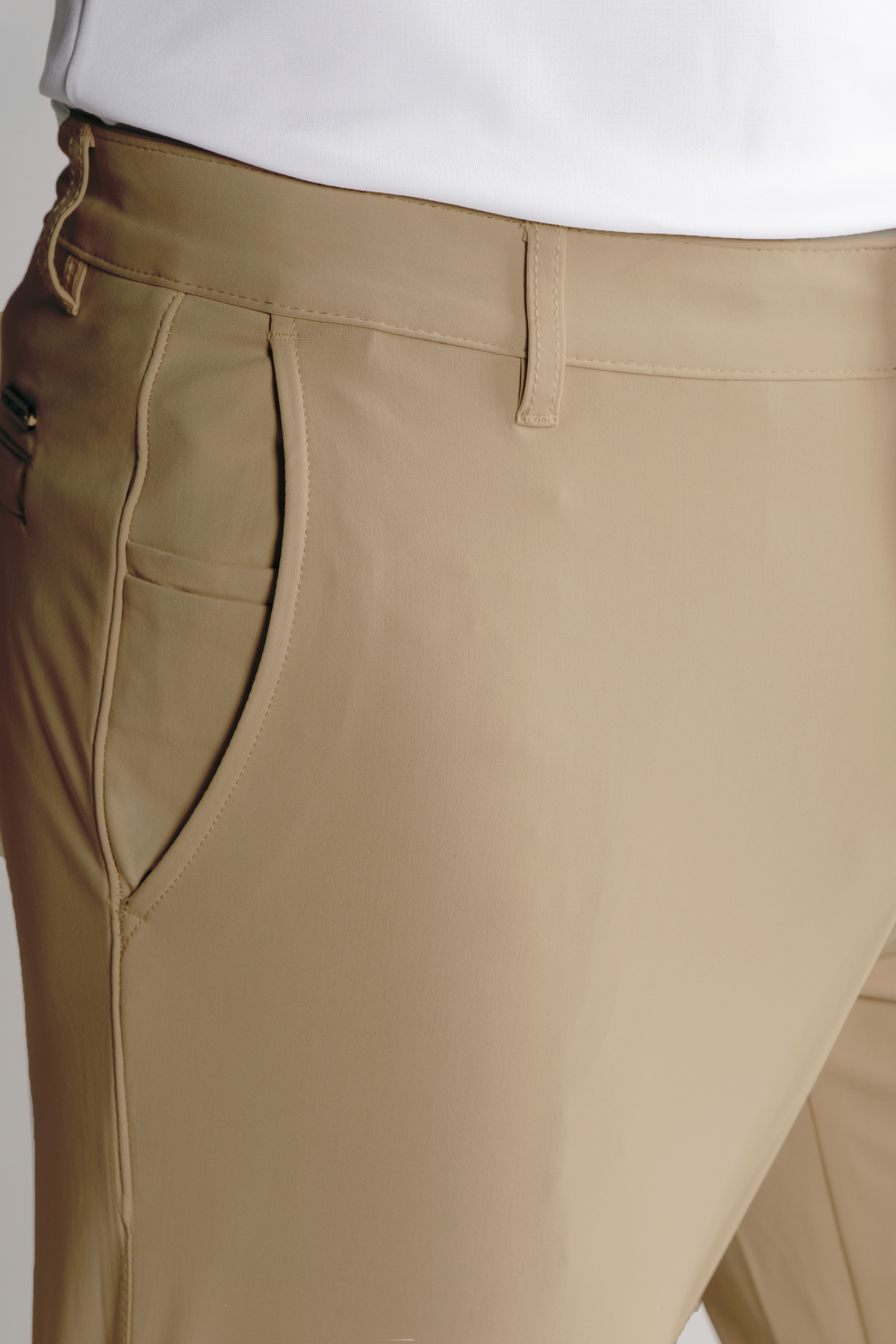 Close-up of a person wearing Twillory Performance Pants // Khaki, featuring non-iron stretch fabric, side pocket, and belt loop. Paired with a tucked-in white shirt, the pants offer comfort and style at the hip and waist.