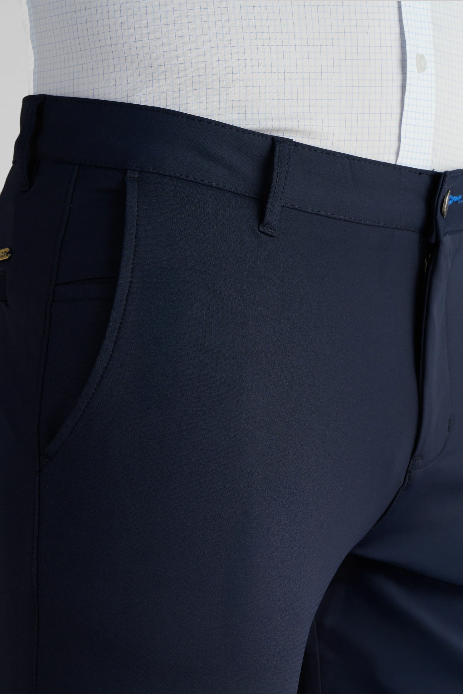 A close-up of a person wearing Twillory's Performance Pants // NAVY—tailored, formal non-iron trousers with side pockets and belt loops—paired with a white checkered shirt featuring subtle blue grid lines.