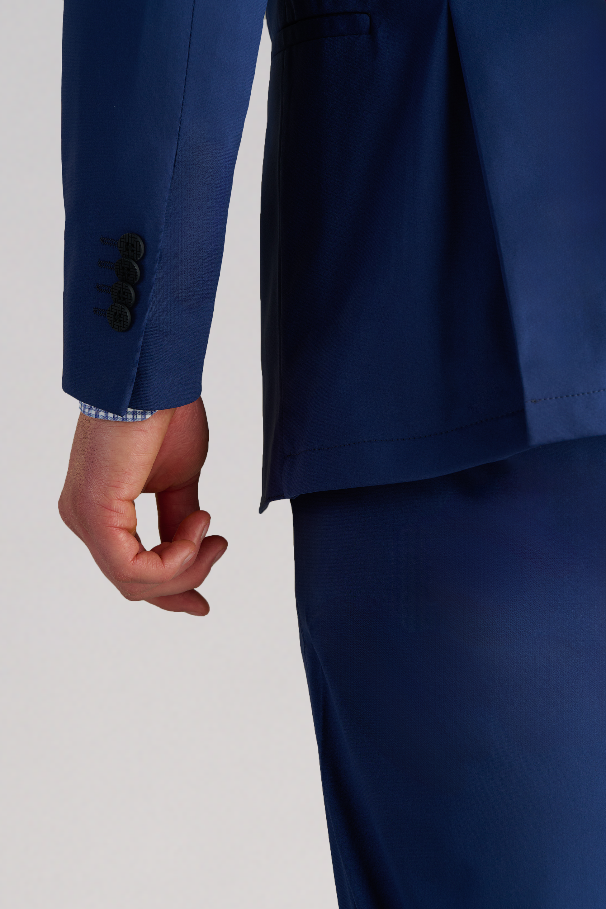 A person wears the Twillory Performance Blazer in Cobalt Blue with matching pants. Their left arm is down, revealing a blue and white check shirt cuff. The background is plain and light-colored.
