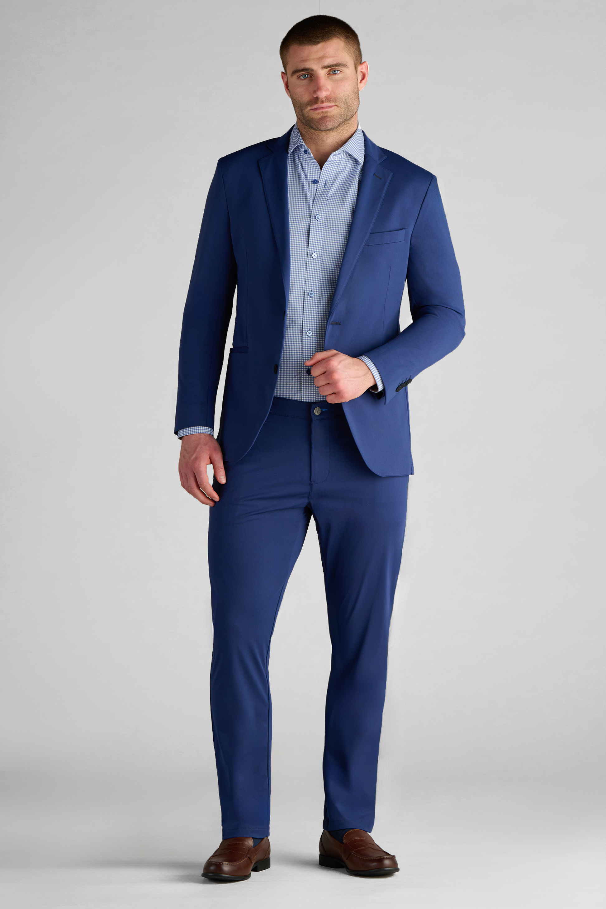 A man with short brown hair and a trimmed beard wears the Twillory Performance Blazer in Cobalt Blue with matching pants, a light blue shirt, and brown dress shoes, standing against a plain light gray background.