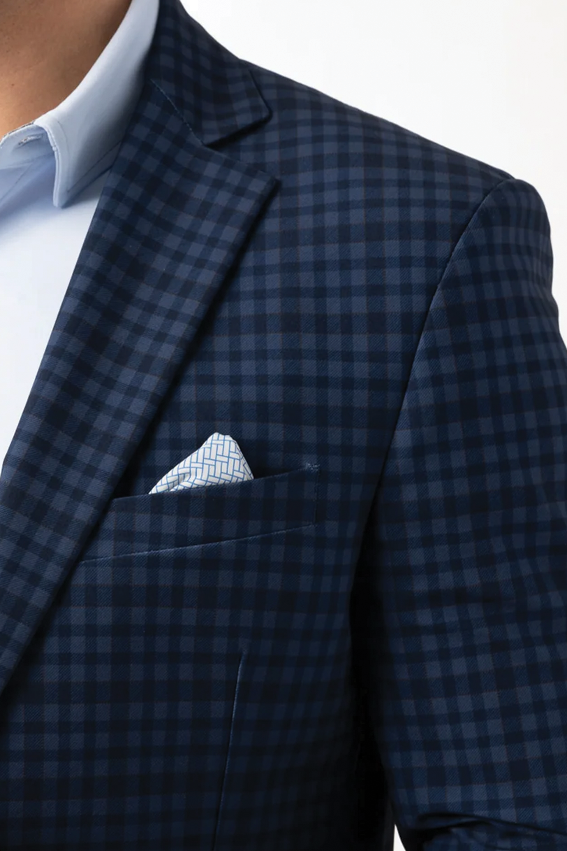 Close-up of a person wearing Twillory's Performance Blazer // Blue Navy Check over a light blue dress shirt, with a white and blue geometric pocket square, set against a plain white background.