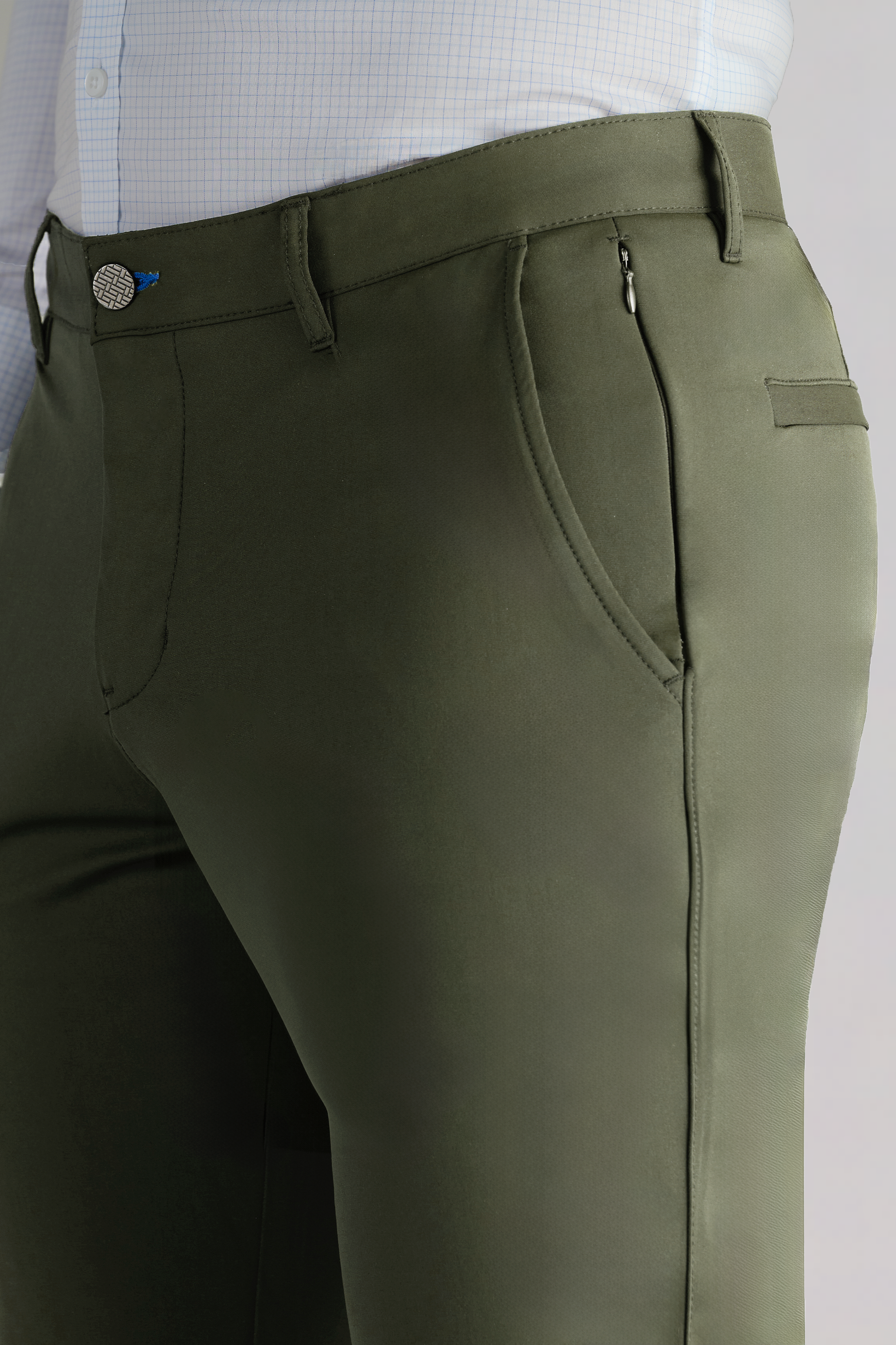 A close-up of Twillory’s Performance Pants // Olive, featuring a side zipper pocket and belt loops, paired with a tucked-in light blue checkered dress shirt. Only the waist and upper thigh area are visible.