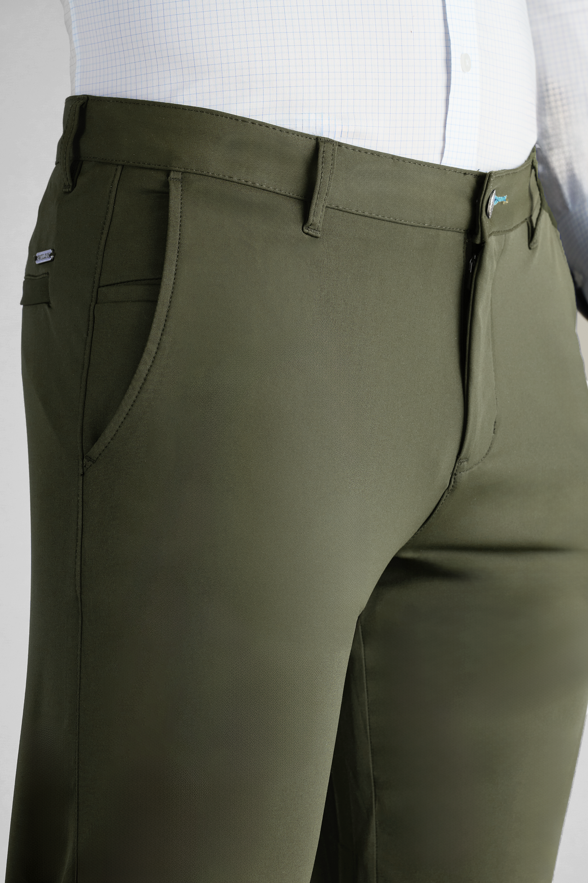 A close-up of a person wearing Twillory Performance Pants // Olive, featuring front pockets and belt loops, styled with a tucked-in white shirt with a subtle grid pattern. The pants have a fitted, tailored look.