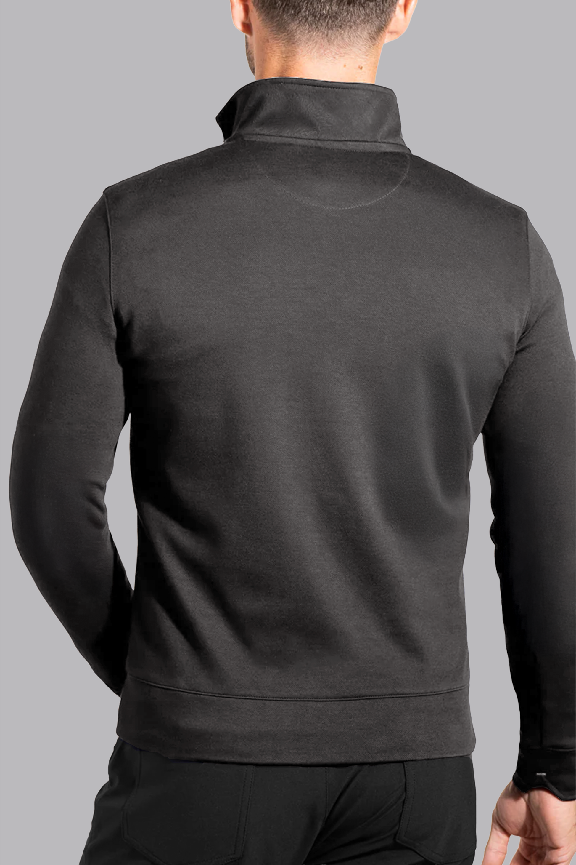A man is seen from behind wearing the Twillory Performance Quarter Zip // Charcoal, featuring a fitted design and stand-up collar. His arms are at his sides as he stands against a plain, light gray background.