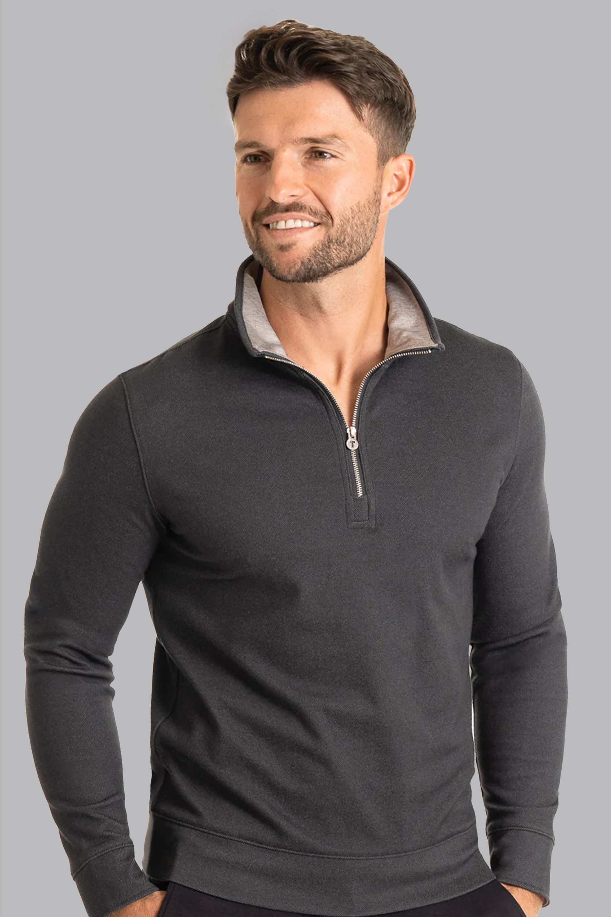 A man with short brown hair and a trimmed beard wears the Twillory Performance Quarter Zip in Charcoal, featuring a light inner collar. He is smiling, looking slightly left, and stands against a plain gray background.