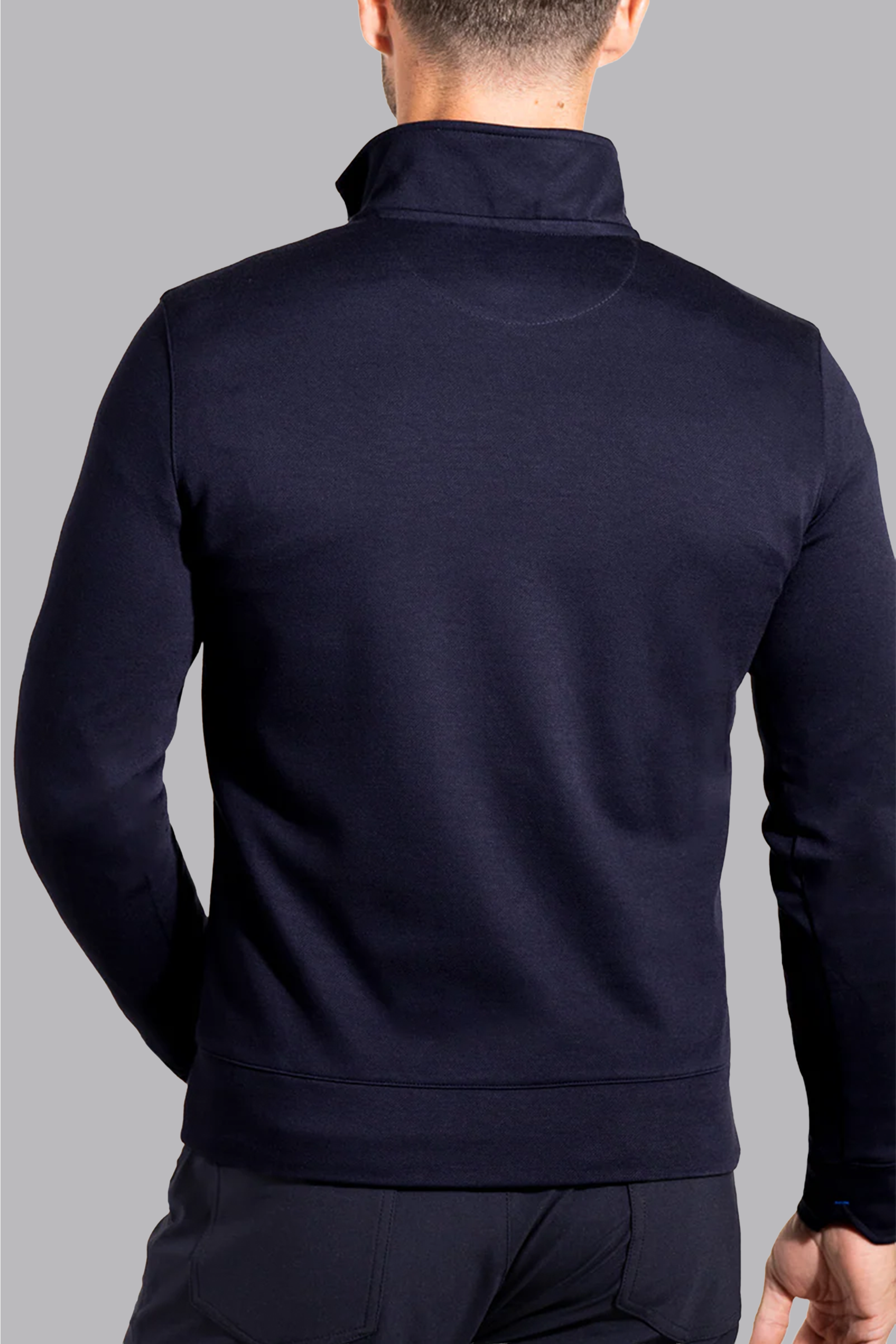 A man is seen from behind wearing the Twillory Performance Quarter Zip // Navy, featuring a high collar, ideal for layering with business casual looks. He stands against a plain light gray background, head slightly turned left and arms at his sides.
