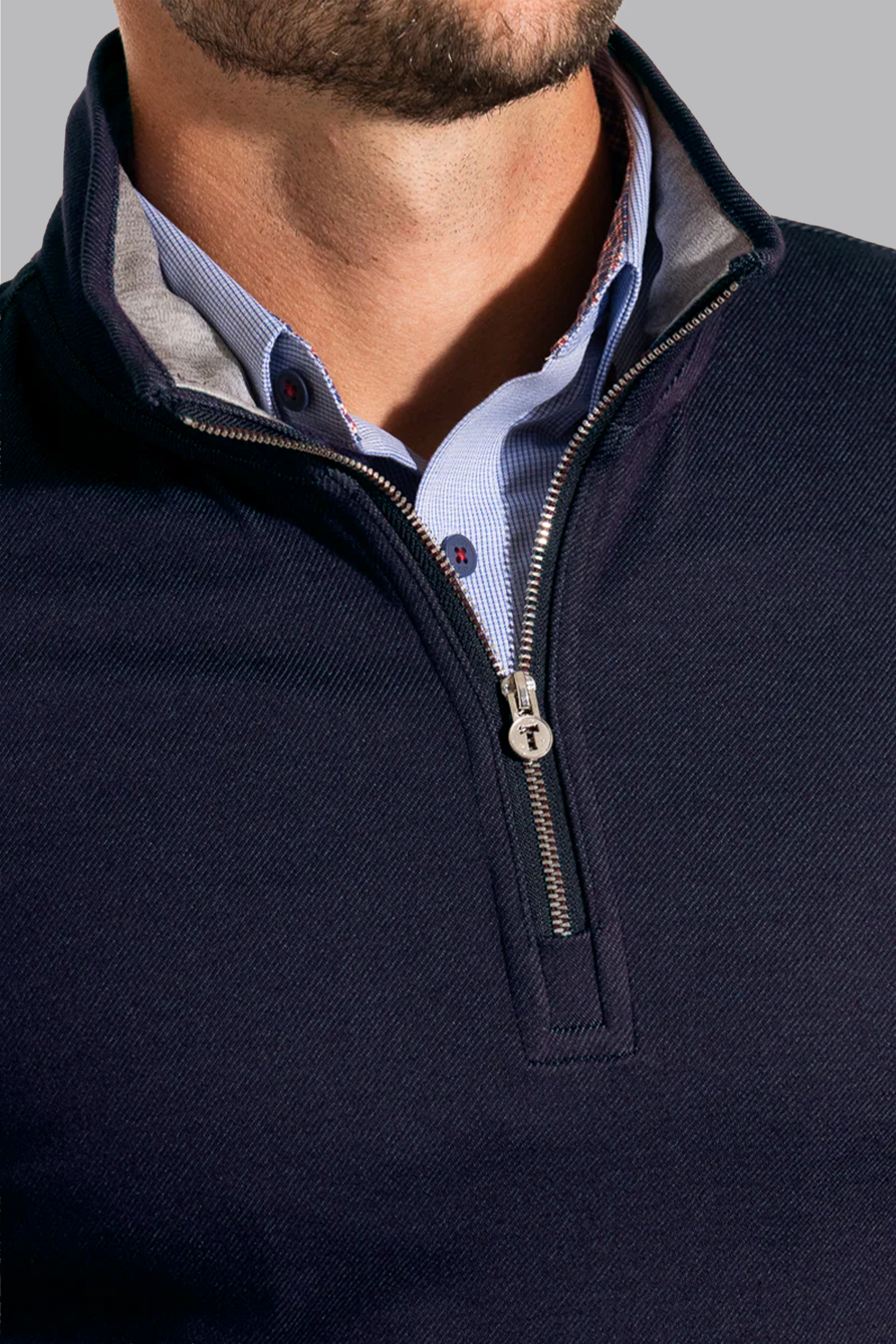 A close-up shows a man wearing the Twillory Performance Quarter Zip in Navy over a light blue button-down shirt. The silver zipper is partly open, revealing the shirt’s collar and buttons, with his lower face and neck visible.