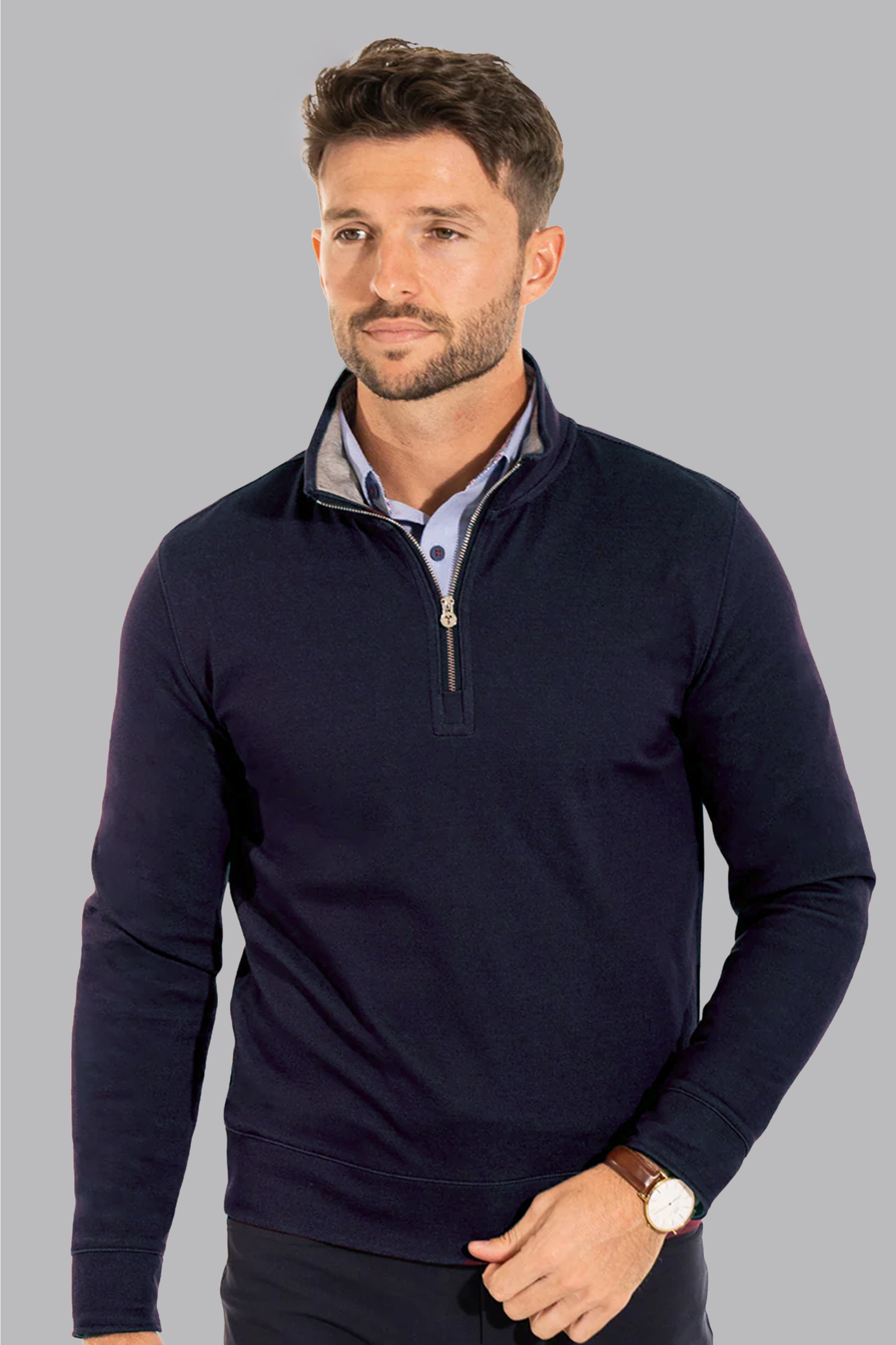 A man with short brown hair and a trimmed beard wears the Twillory Performance Quarter Zip in navy over a light blue collared shirt. He stands against a plain grey background, looking slightly left, wearing a brown watch on his left wrist.