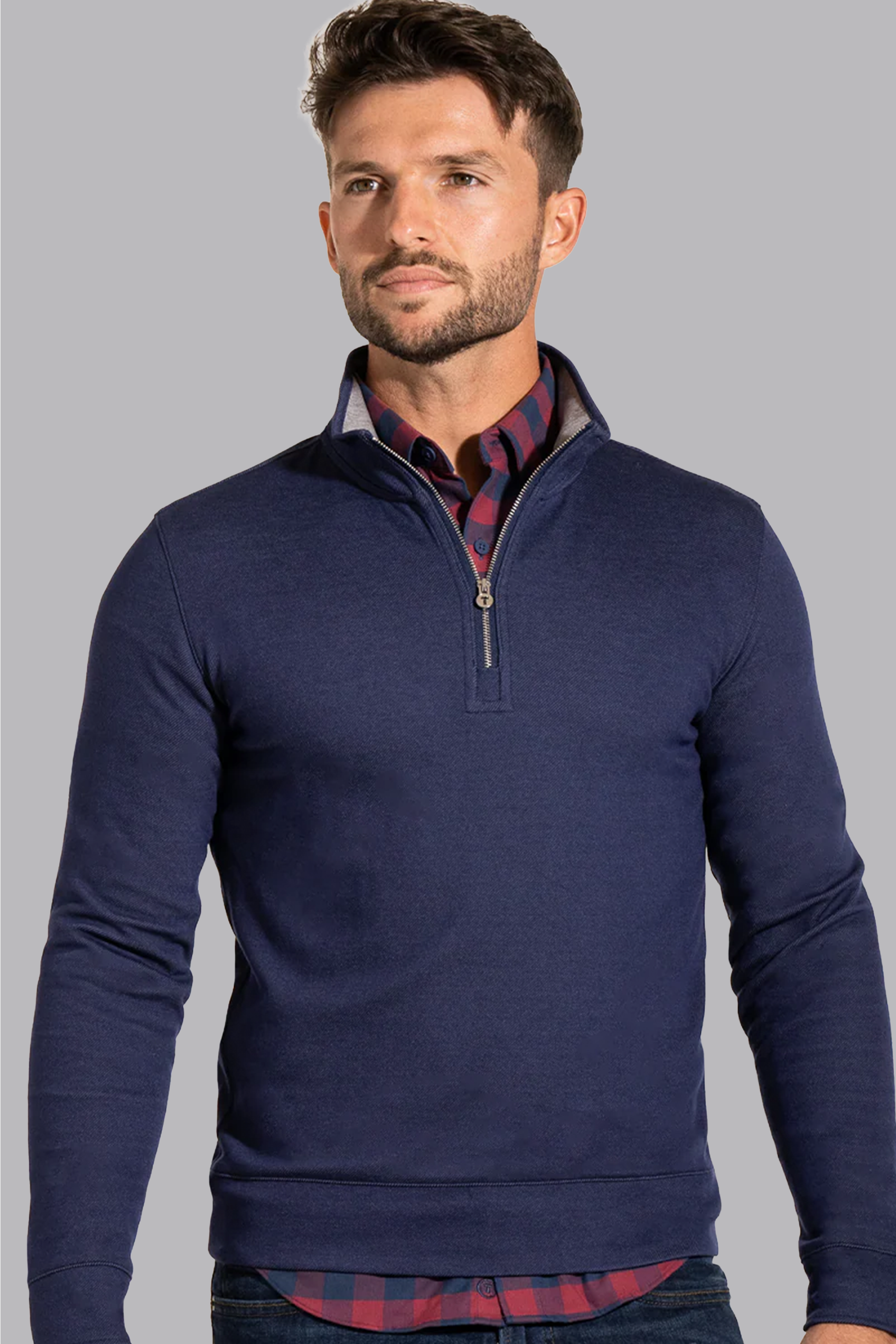A man with short brown hair and a trimmed beard wears the Twillory Performance Quarter Zip in Denim over a red and navy plaid shirt, standing against a plain light gray background, facing forward with a neutral expression and hands by his sides.