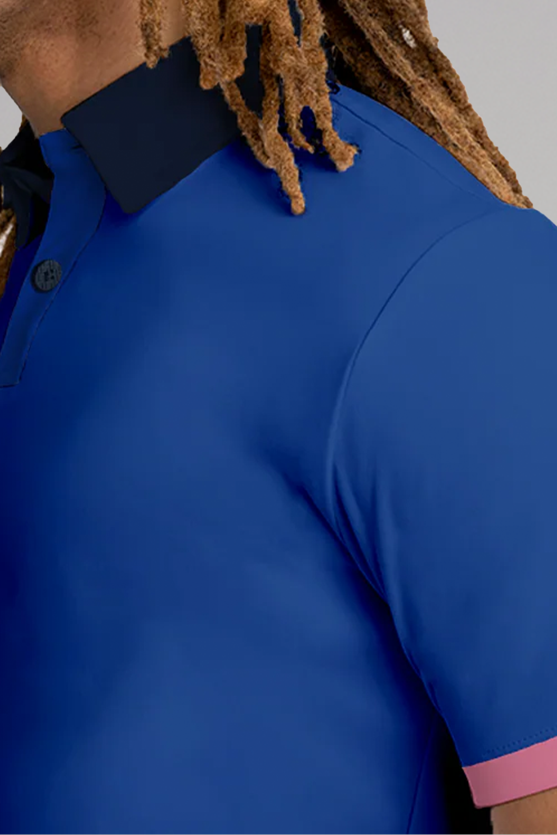 Close-up of a person in the Twillory Short Sleeve Polo Contrast // Blue Pink—a wrinkle-free, moisture-wicking shirt with a navy collar and pink sleeve trim. Only part of their face, shoulder, and upper body appear against a neutral background.