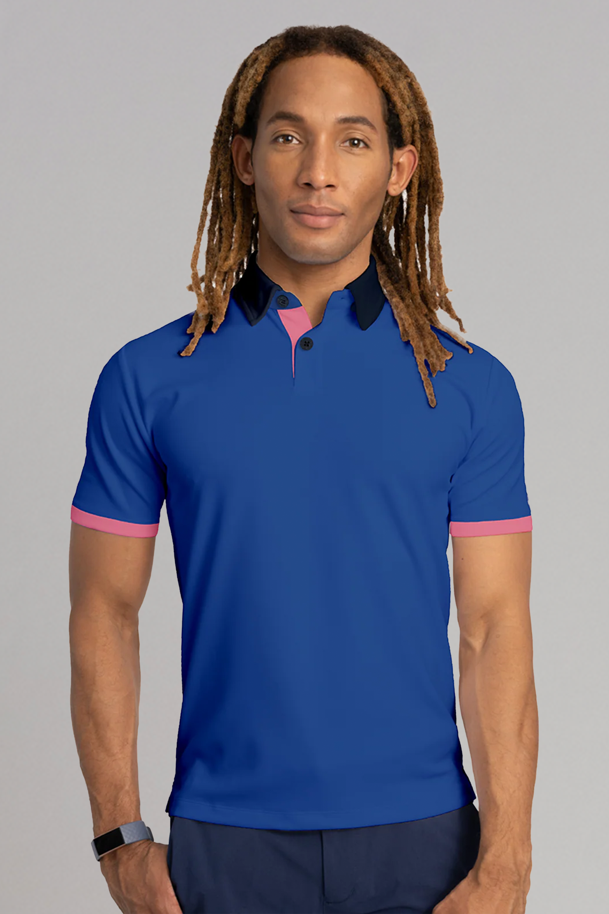 A person with long, light brown dreadlocks wears the Twillory Short Sleeve Polo Contrast // Blue Pink, standing against a plain gray background with a neutral expression and a black wristband.