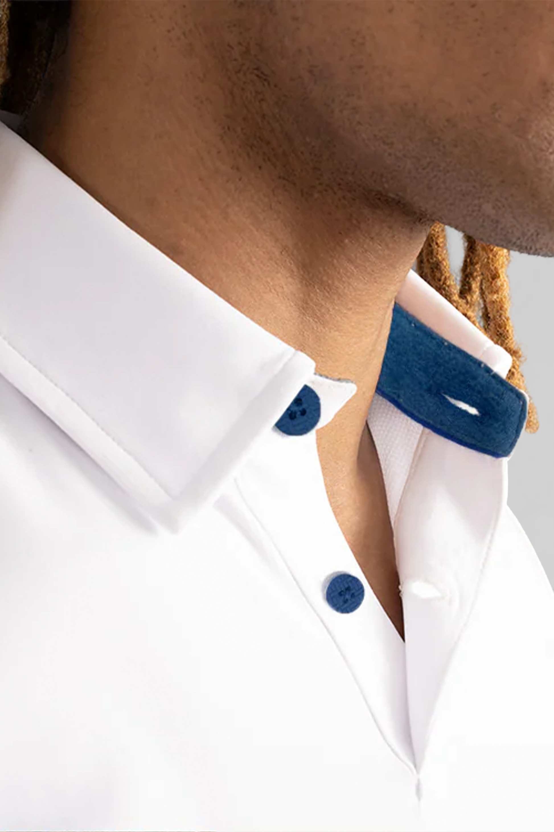 Close-up of a person wearing the Twillory Short Sleeve Polo Contrast in White Blue, featuring a crisp tailored fit, blue buttons, and a contrasting blue collar. Medium brown skin and light brown twisted hair are partially visible.