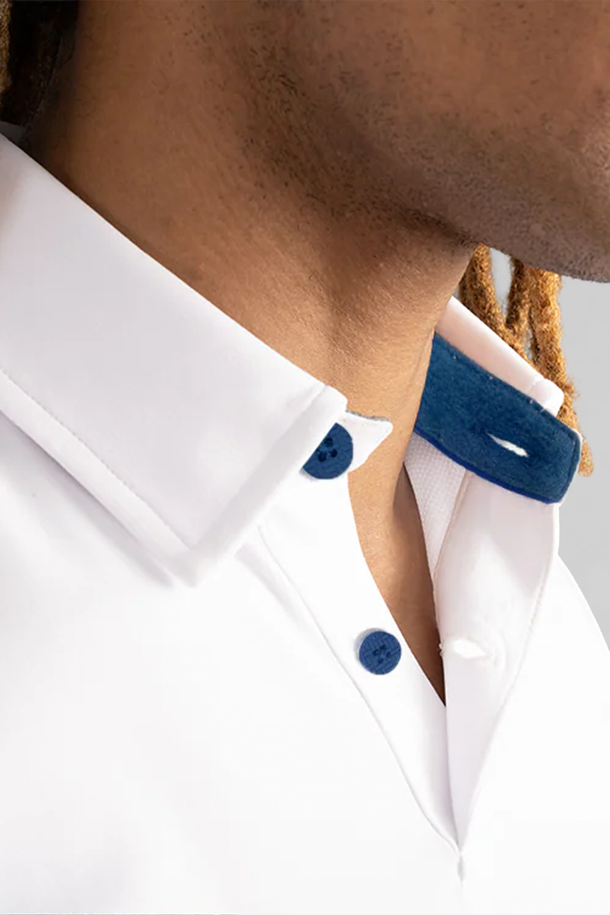 Close-up of a person wearing the Twillory Short Sleeve Polo Contrast in White Blue, featuring a crisp tailored fit, blue buttons, and a contrasting blue collar. Medium brown skin and light brown twisted hair are partially visible.